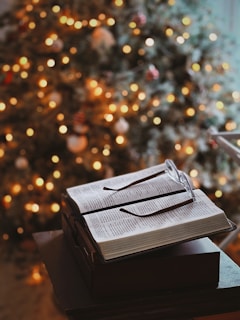 Open book with glasses on blurred christmas tree background