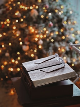 Open book with glasses on blurred christmas tree background