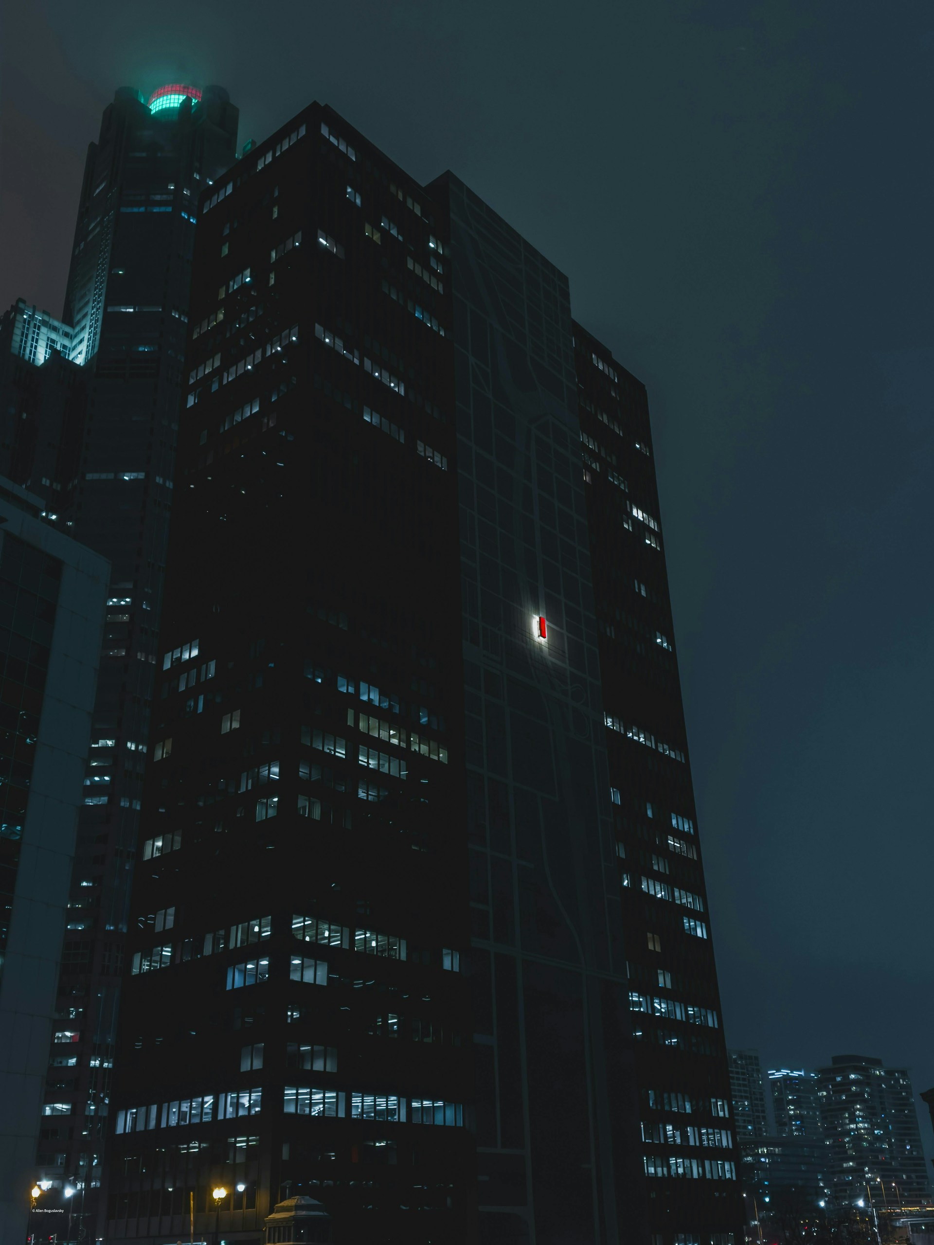 Dark skyscrapers illuminated at night under a cloudy sky.