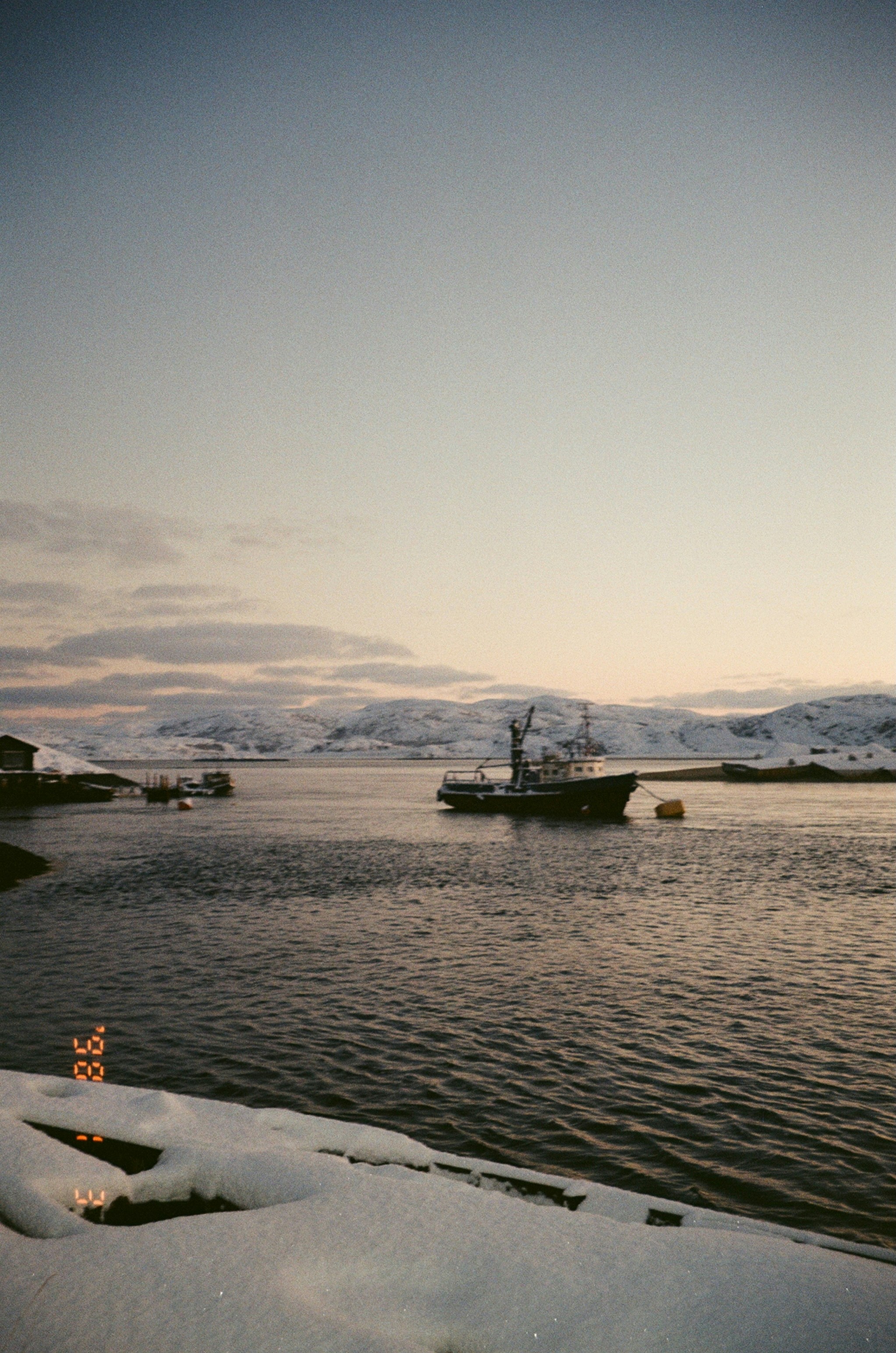 Fishing boat sails on calm water near snowy mountains.