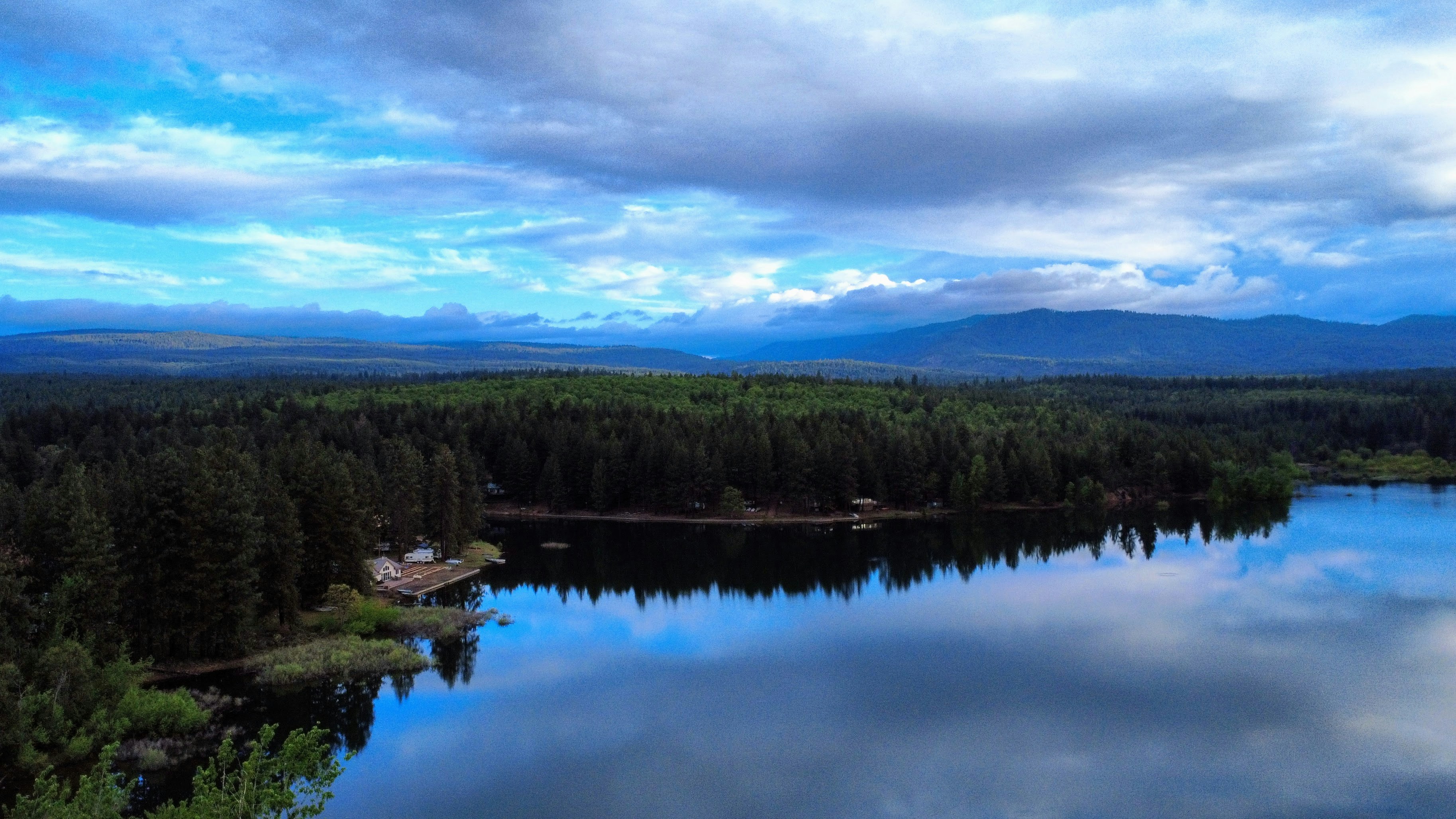 Calm lake reflects dramatic cloudy sky over forest.