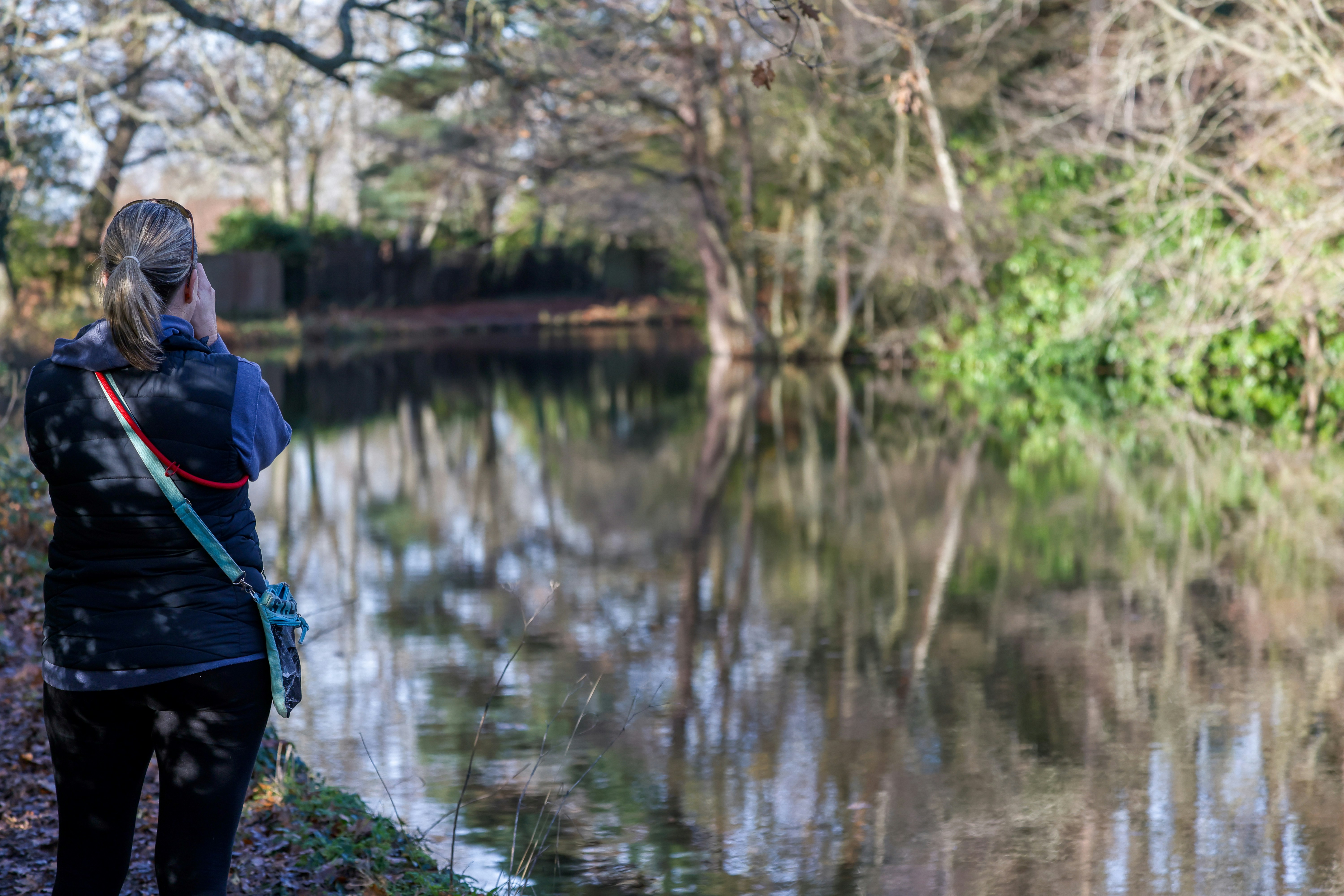 Woman walking beside a calm canal in autumn.