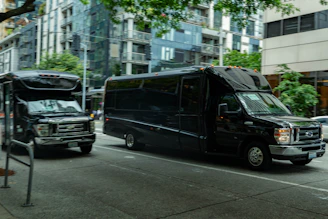 Two black buses driving on a city street.