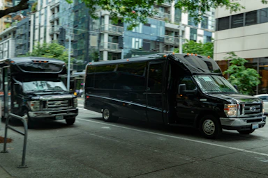 Two black buses driving on a city street.