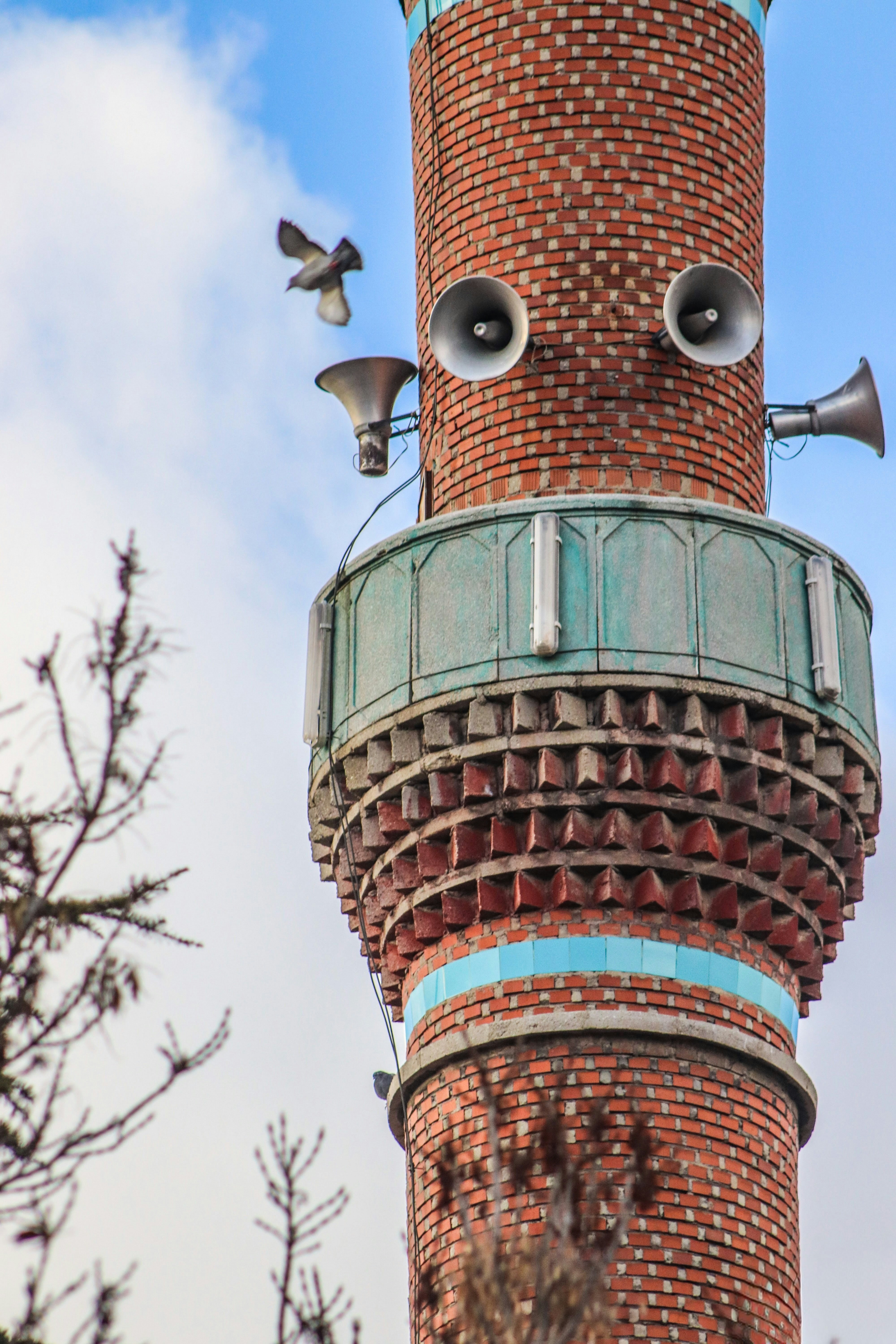 A bird flies near a brick minaret with speakers.