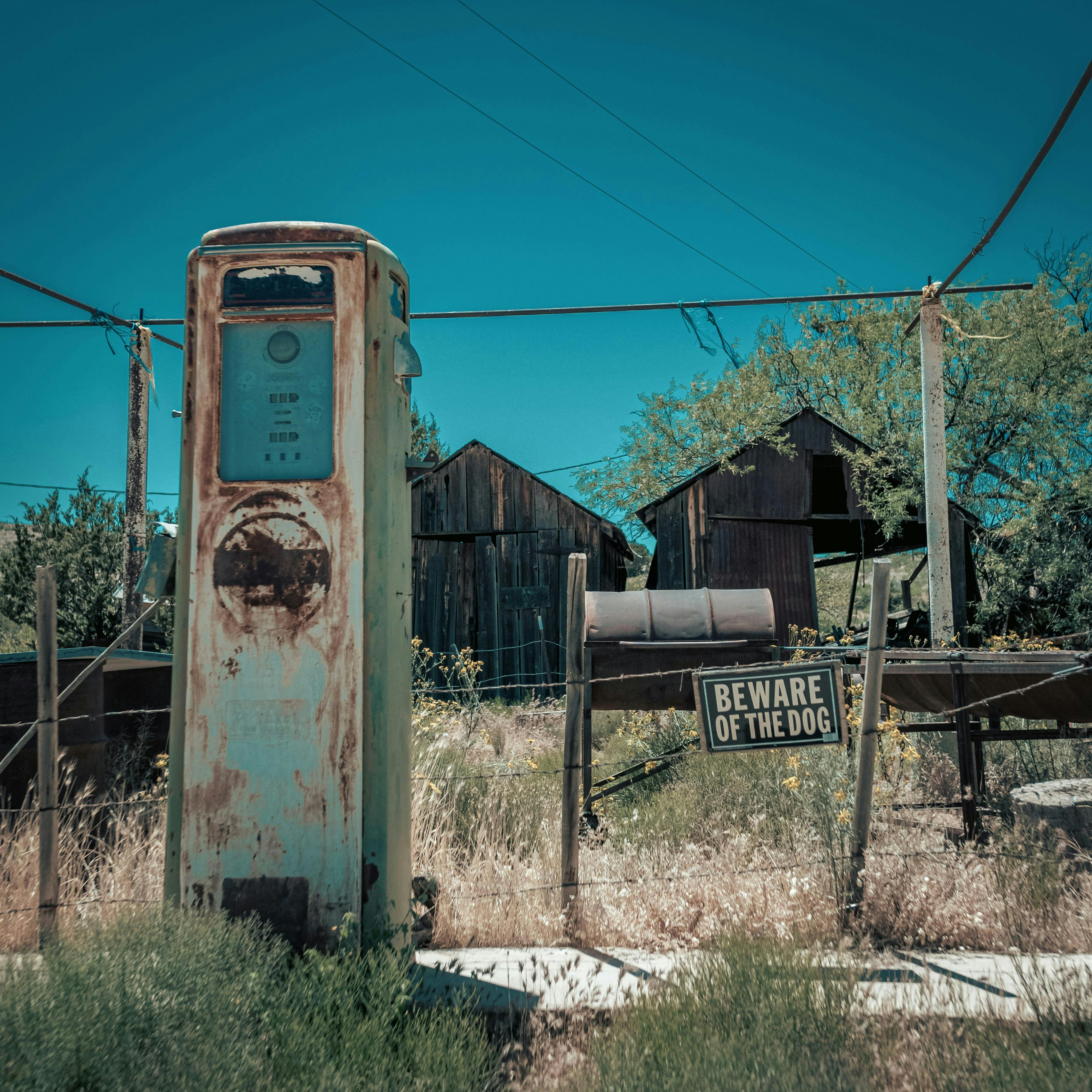 Rusty vintage gas pump in overgrown abandoned lot.