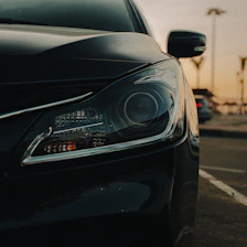 Close-up of a black car's headlight at sunset.