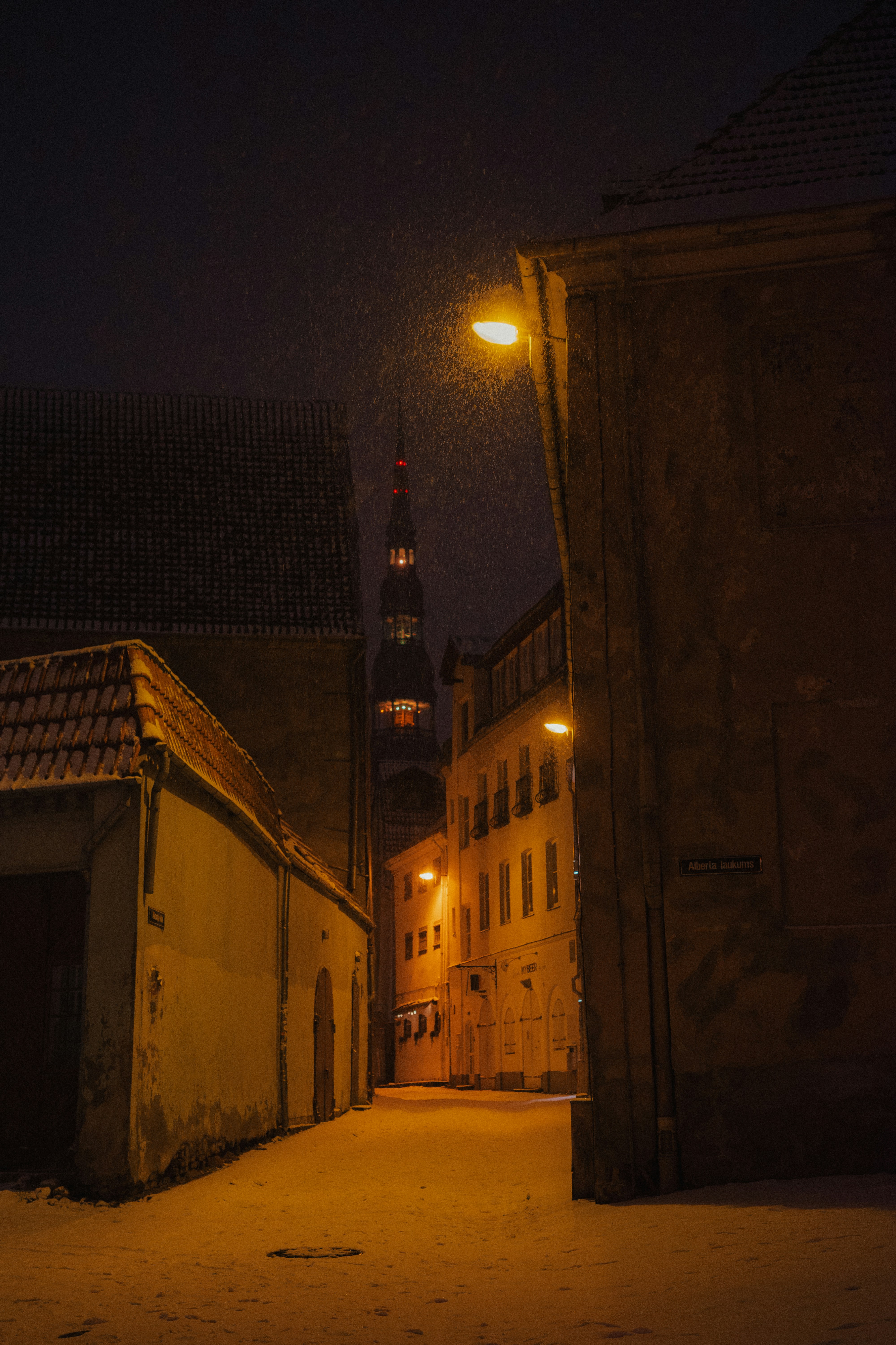 Snowy street at night with illuminated buildings and dark buildings.