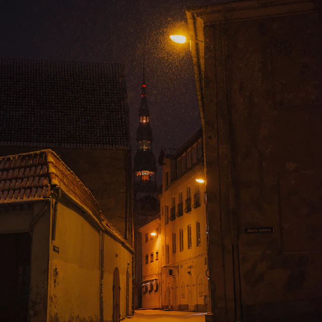 A snowy street at night in Riga with lit and dark buildings