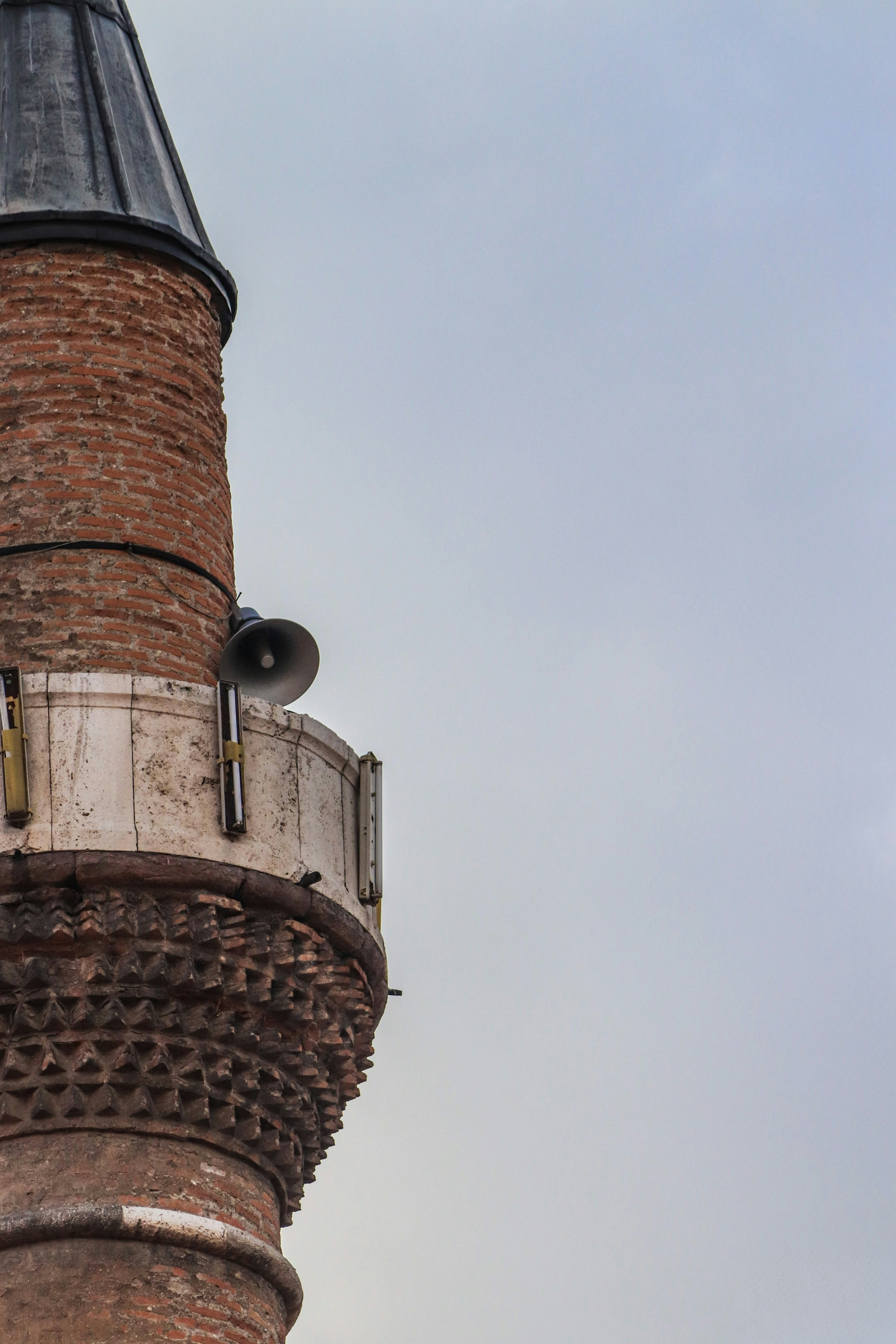 Close-up of a brick minaret with a speaker.