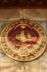 Ornate circular emblem with gold calligraphy and floral details.