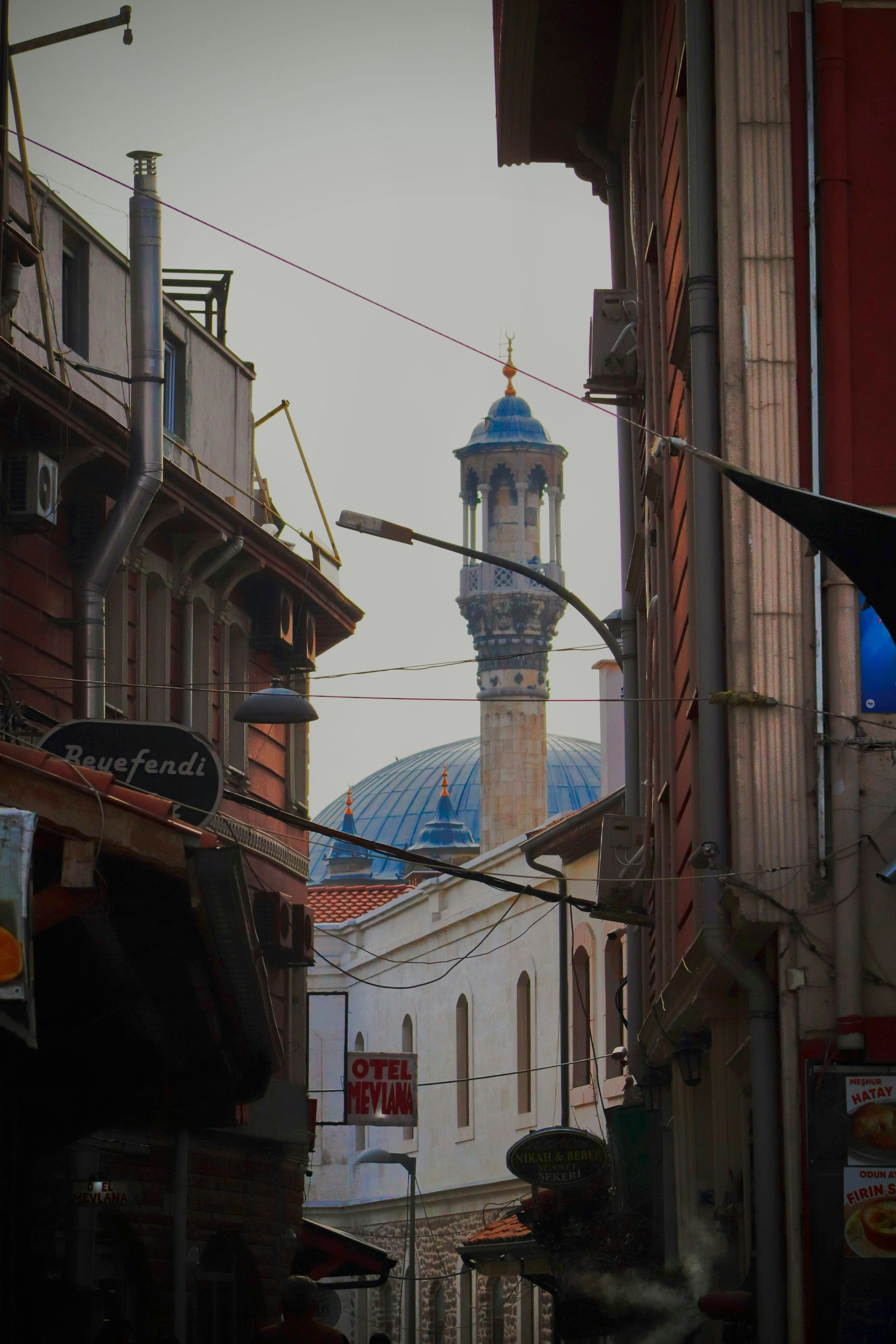 Mosque with blue dome and minaret seen between buildings.