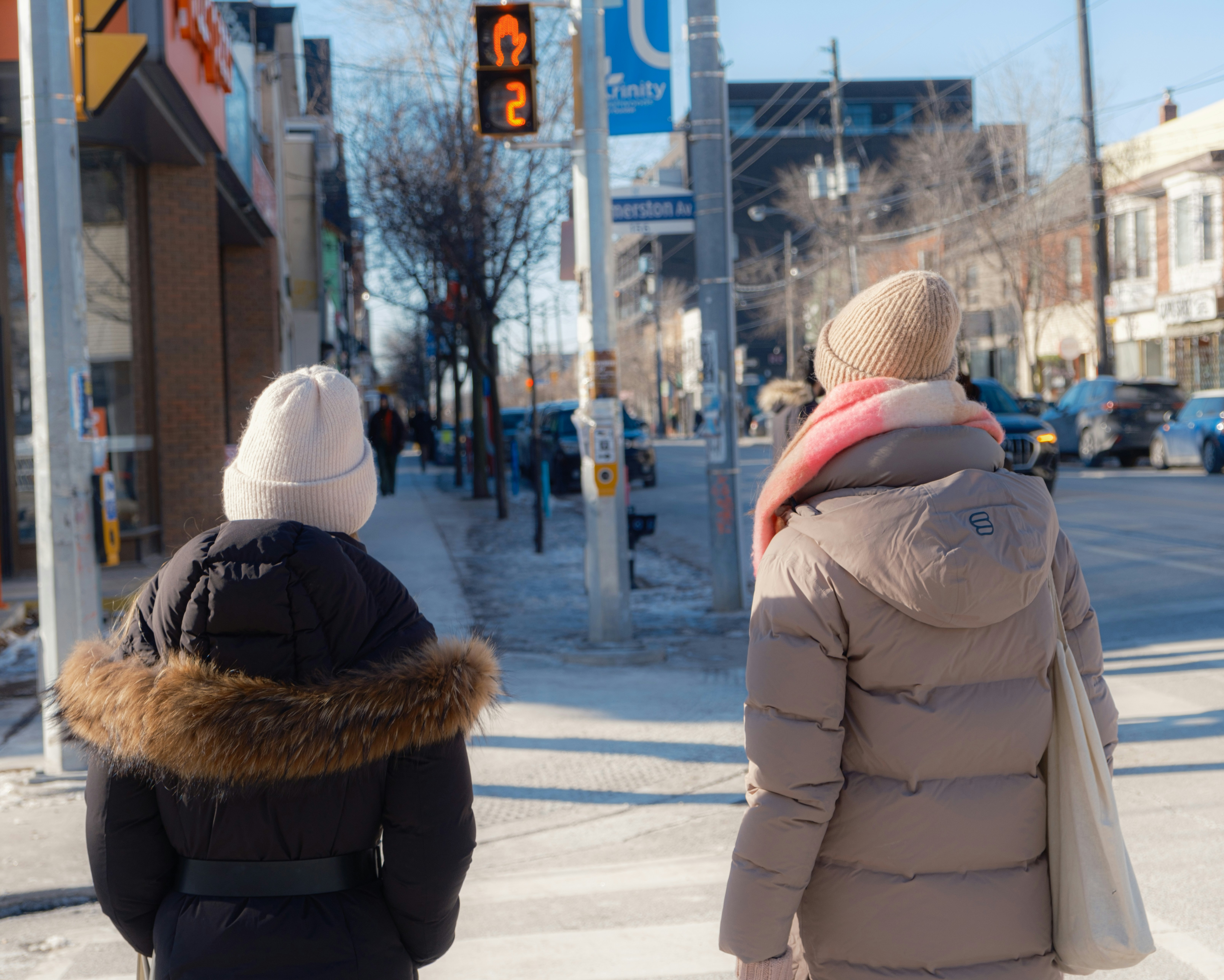 Two people walk across a snowy city street.