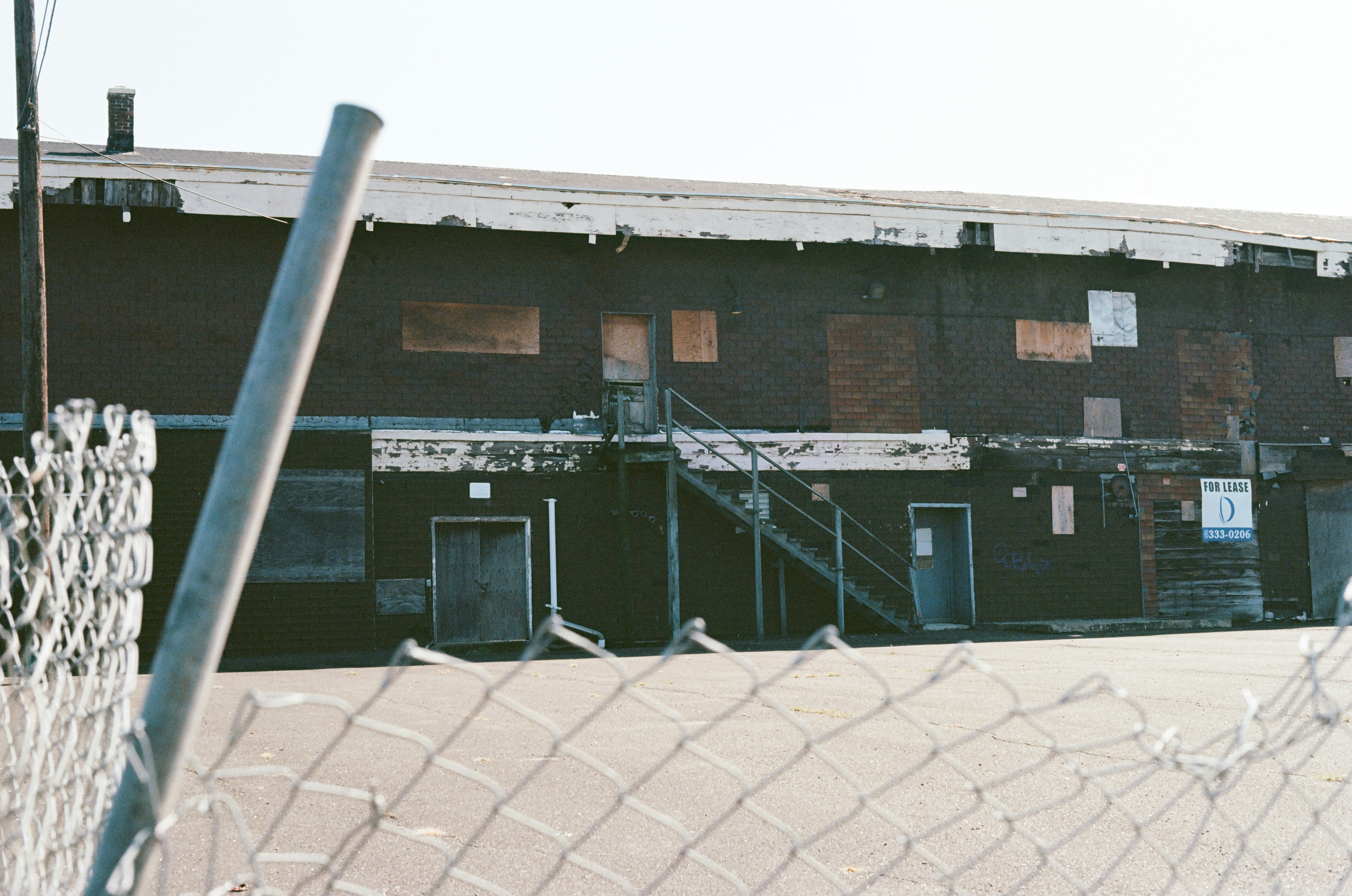Dark brick building with boarded windows and metal stairs.