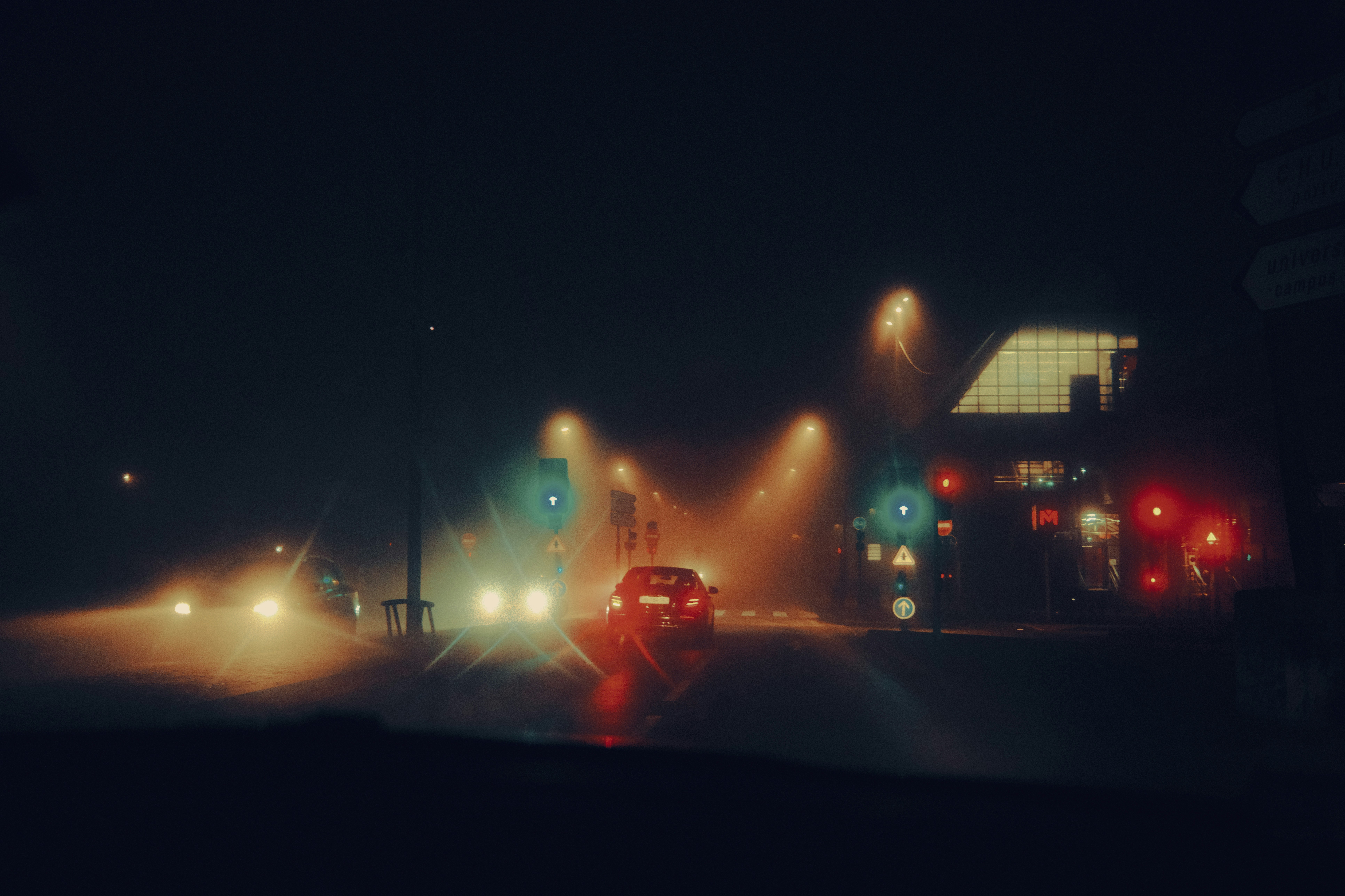 Cars driving on a foggy road at night.