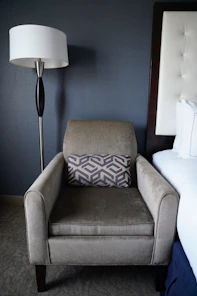 Armchair with decorative pillow next to a bed.