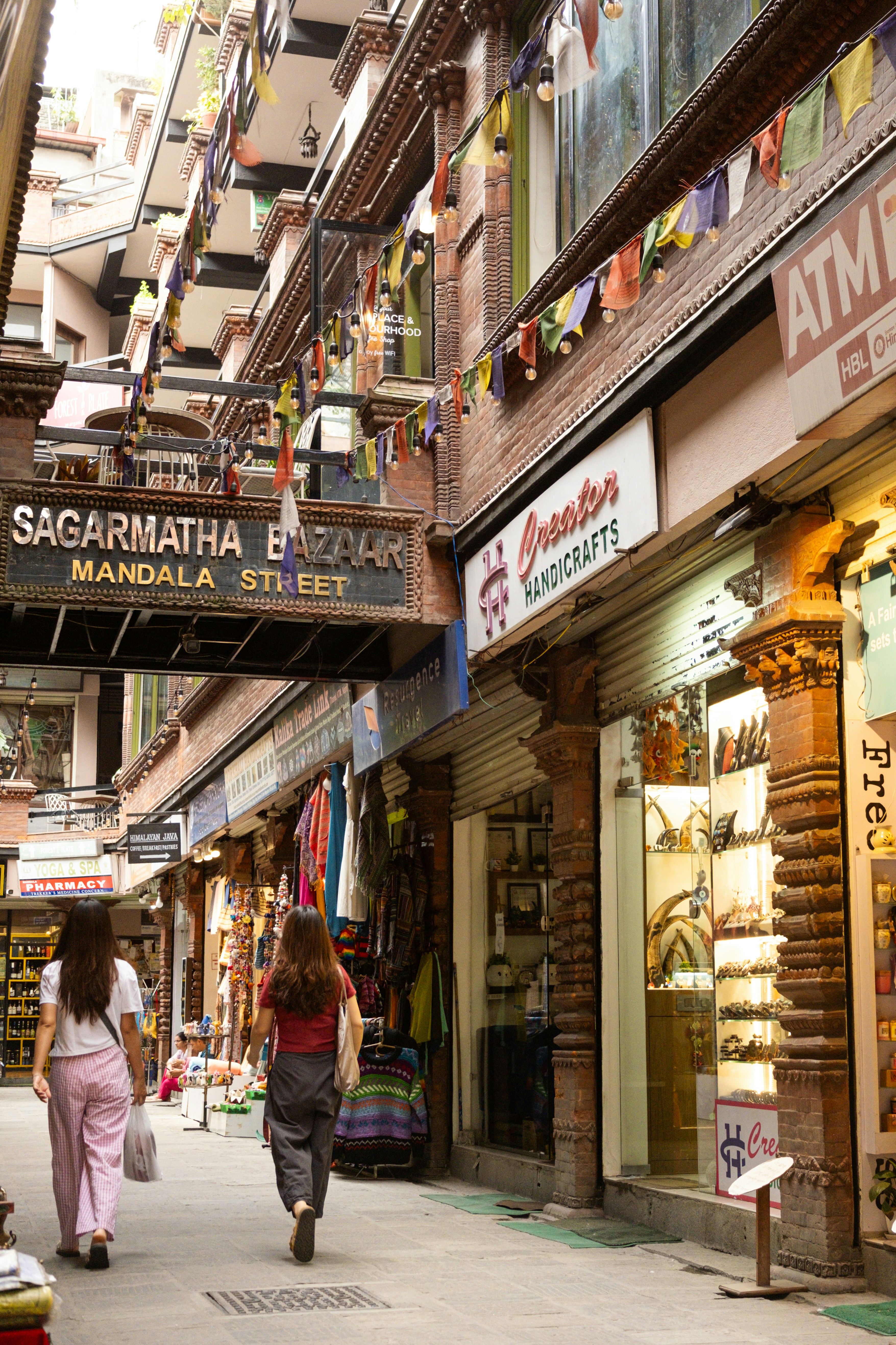 Two women walk down a narrow street lined with shops.