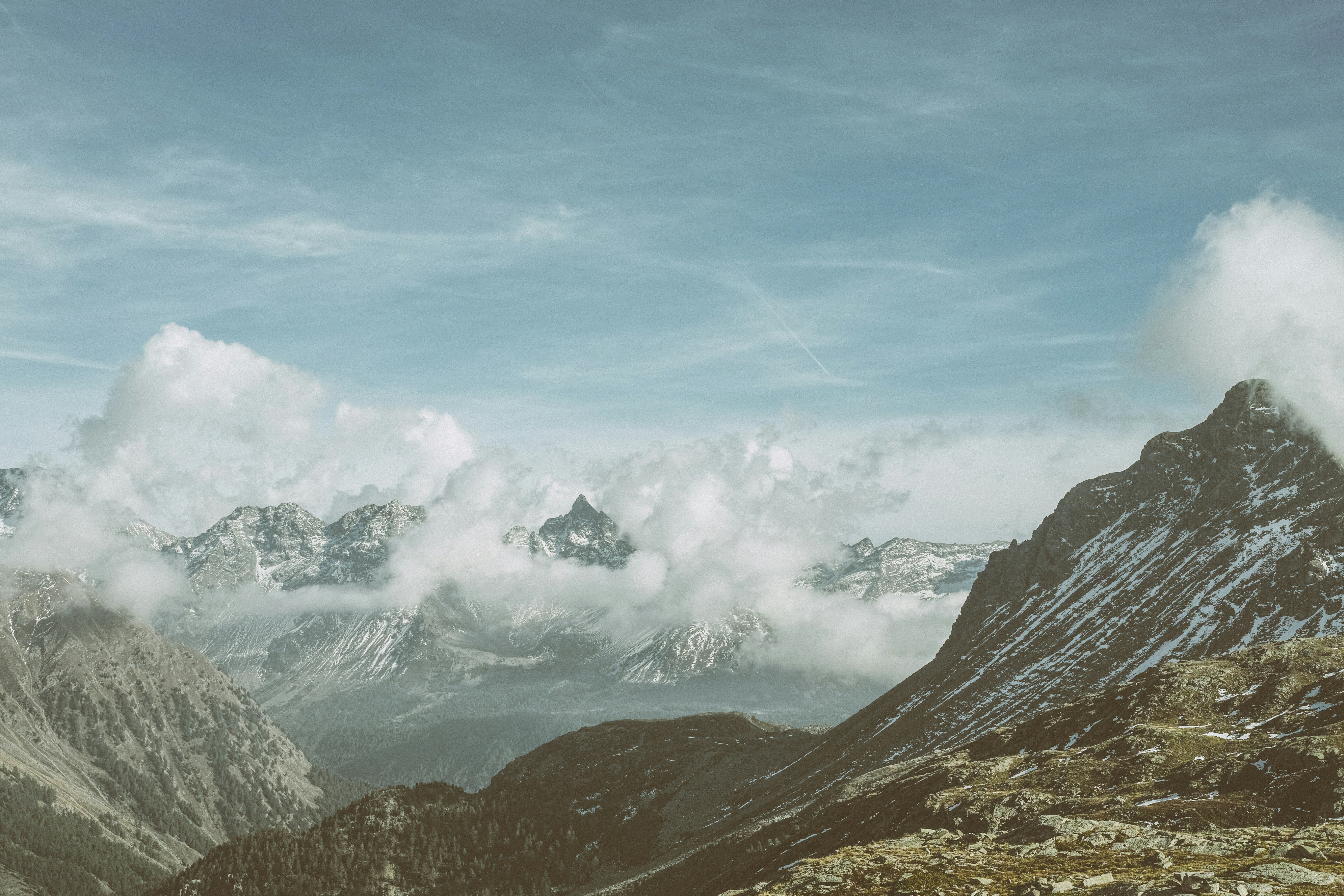 Snow-capped mountains shrouded in clouds under a blue sky.