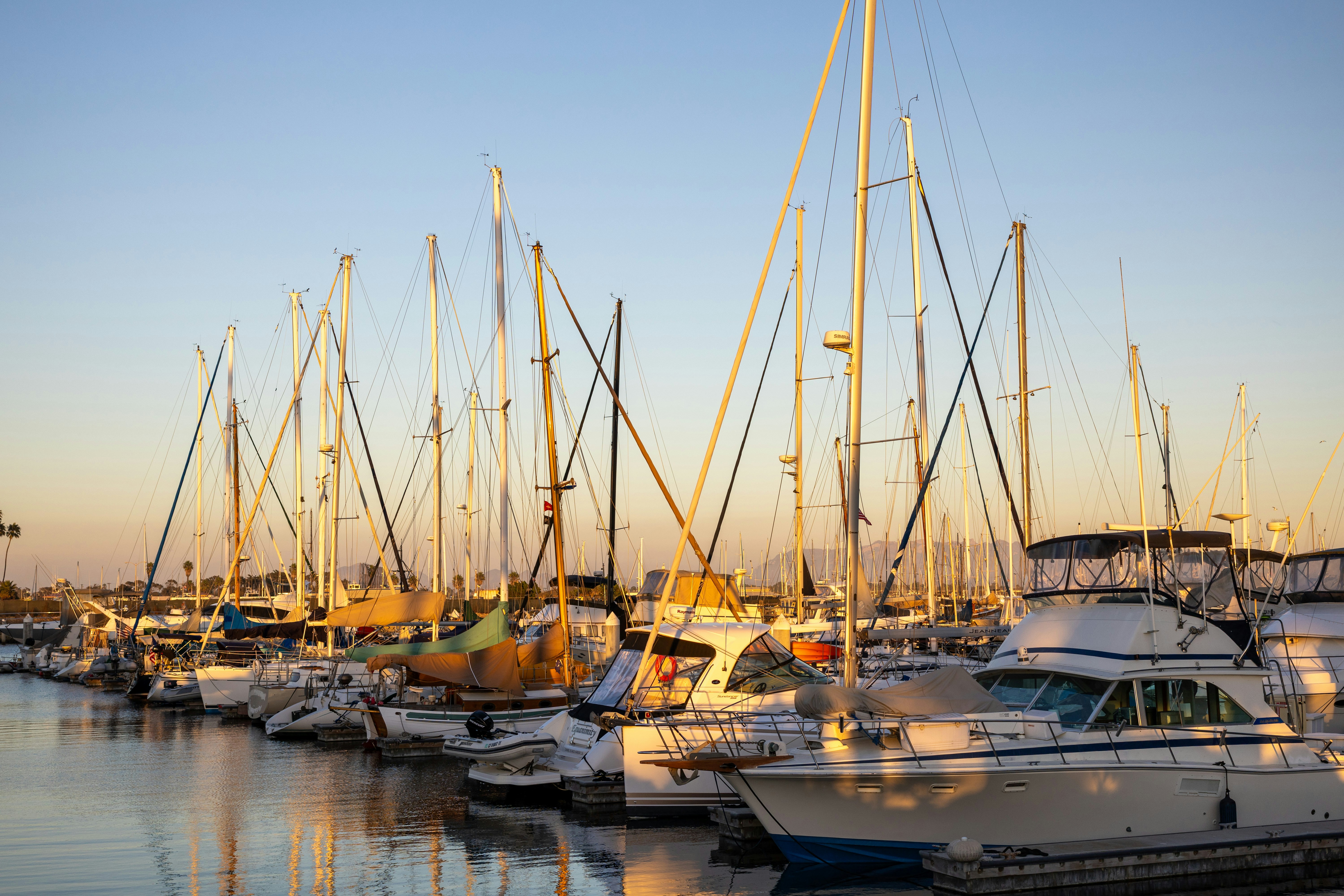 Sailboats and yachts docked in a marina at sunset.