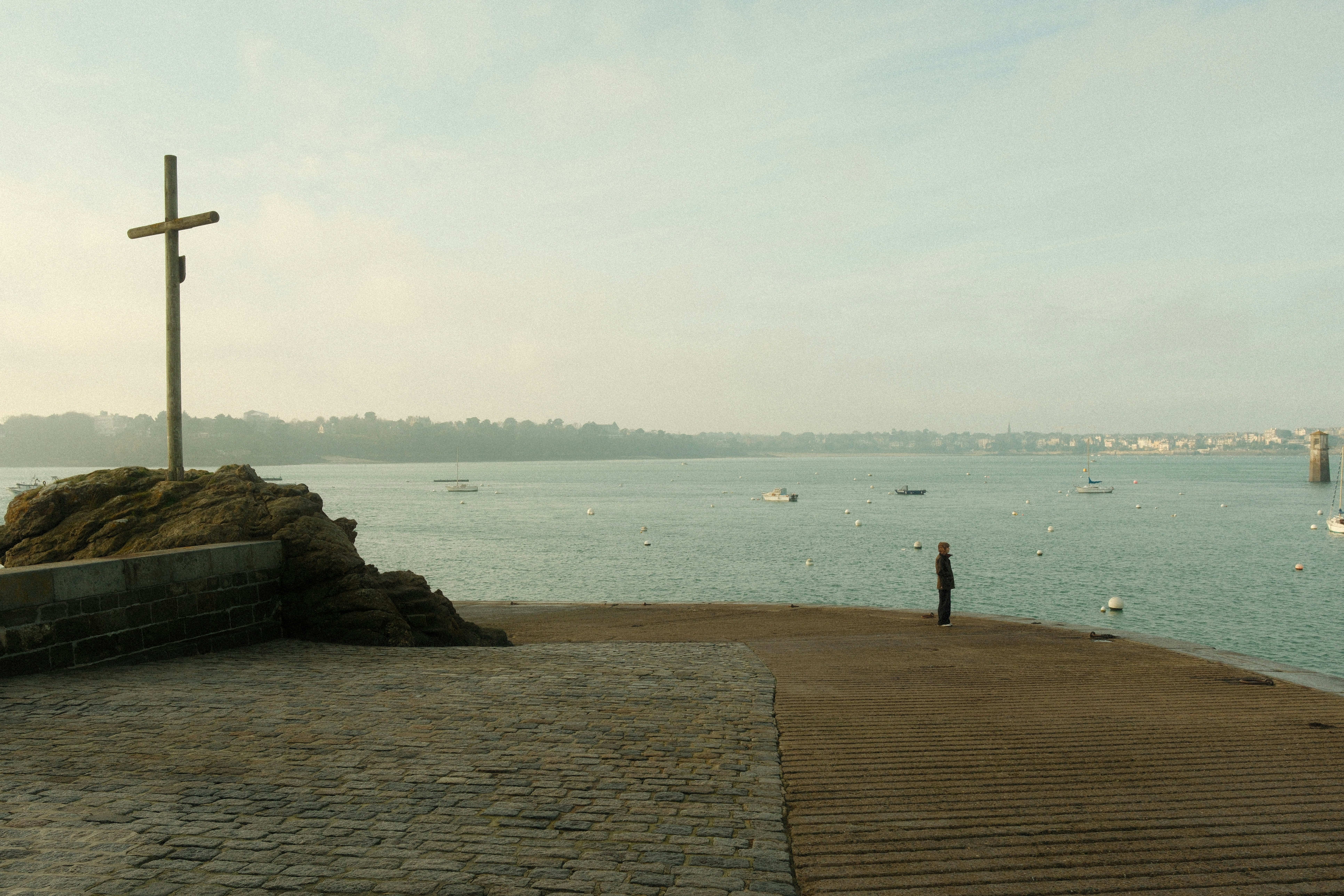 A lone figure stands by a cross overlooking the sea