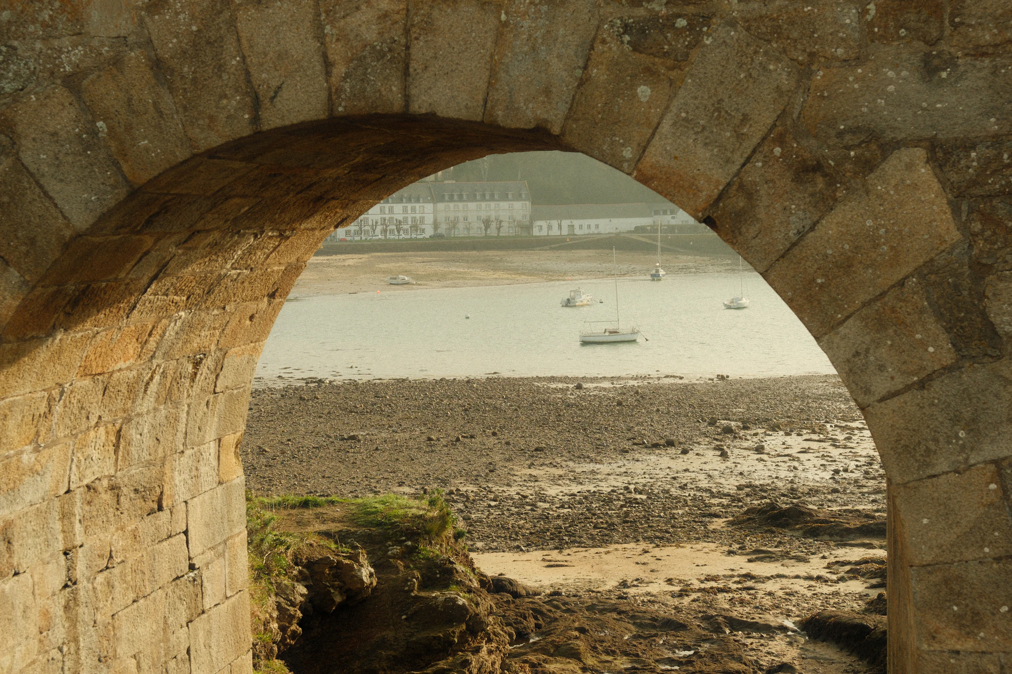 An old stone archway framing boats on a calm bay