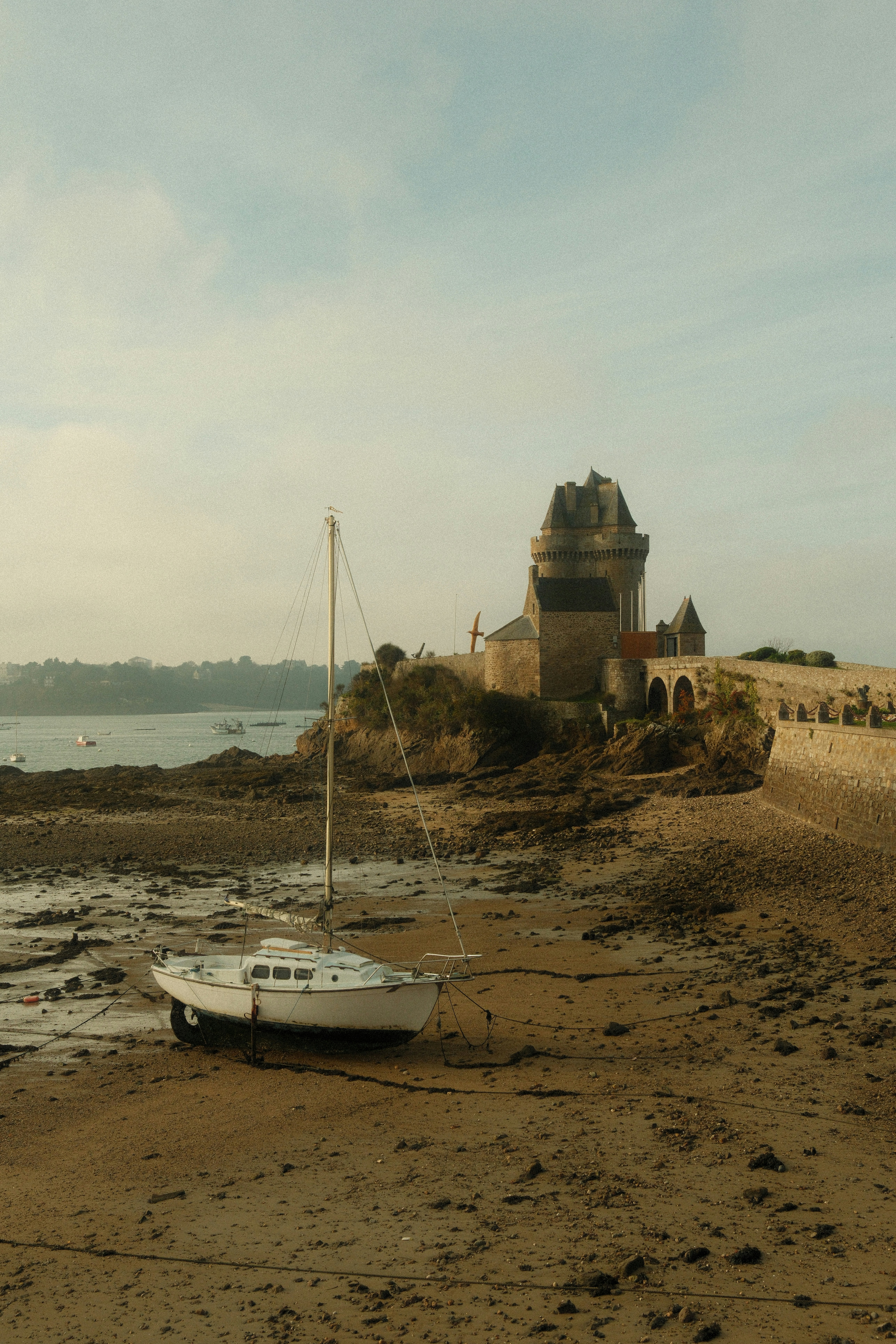 Sailboat resting on a muddy shore near a stone building.