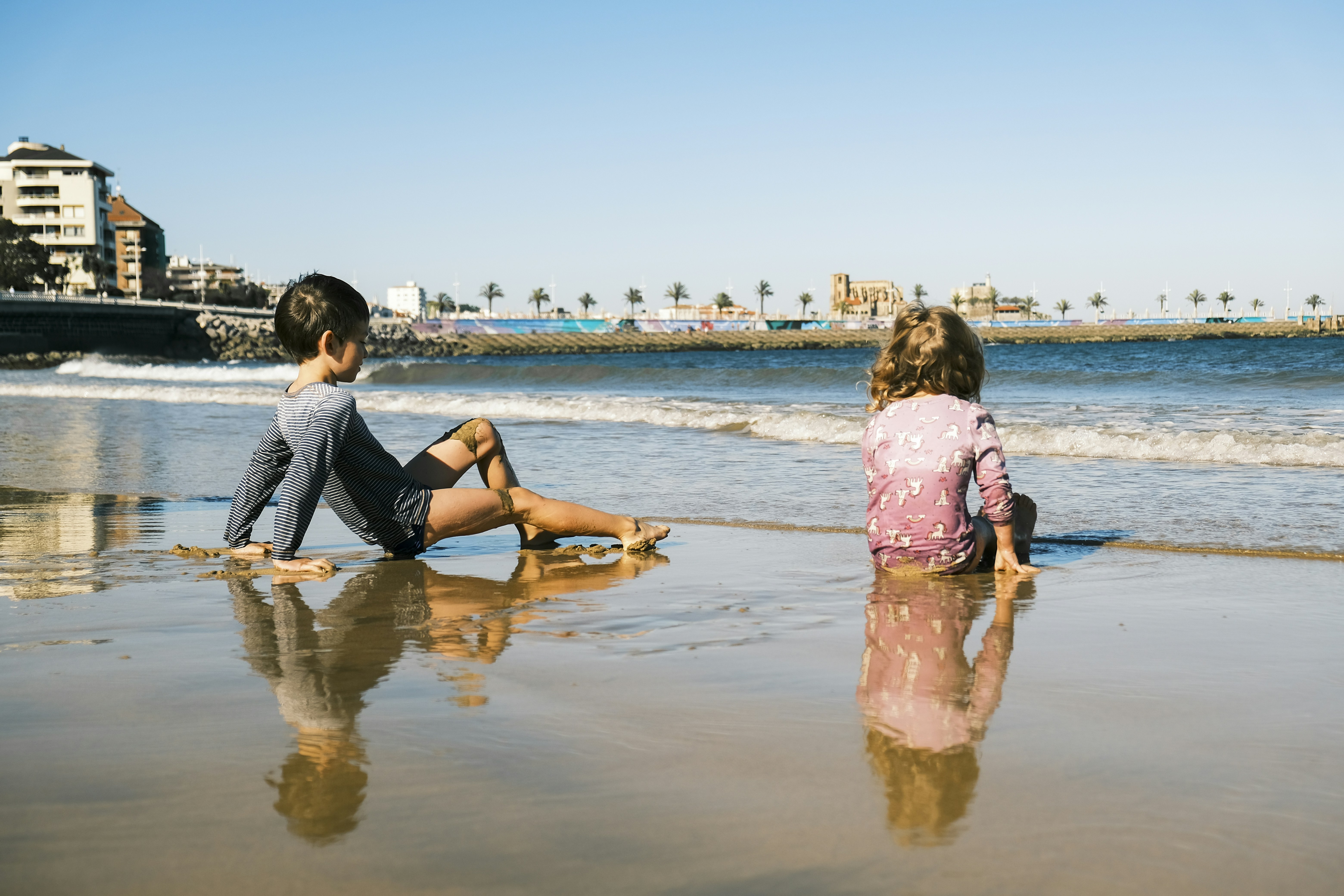 Two children sitting on a wet sandy beach.