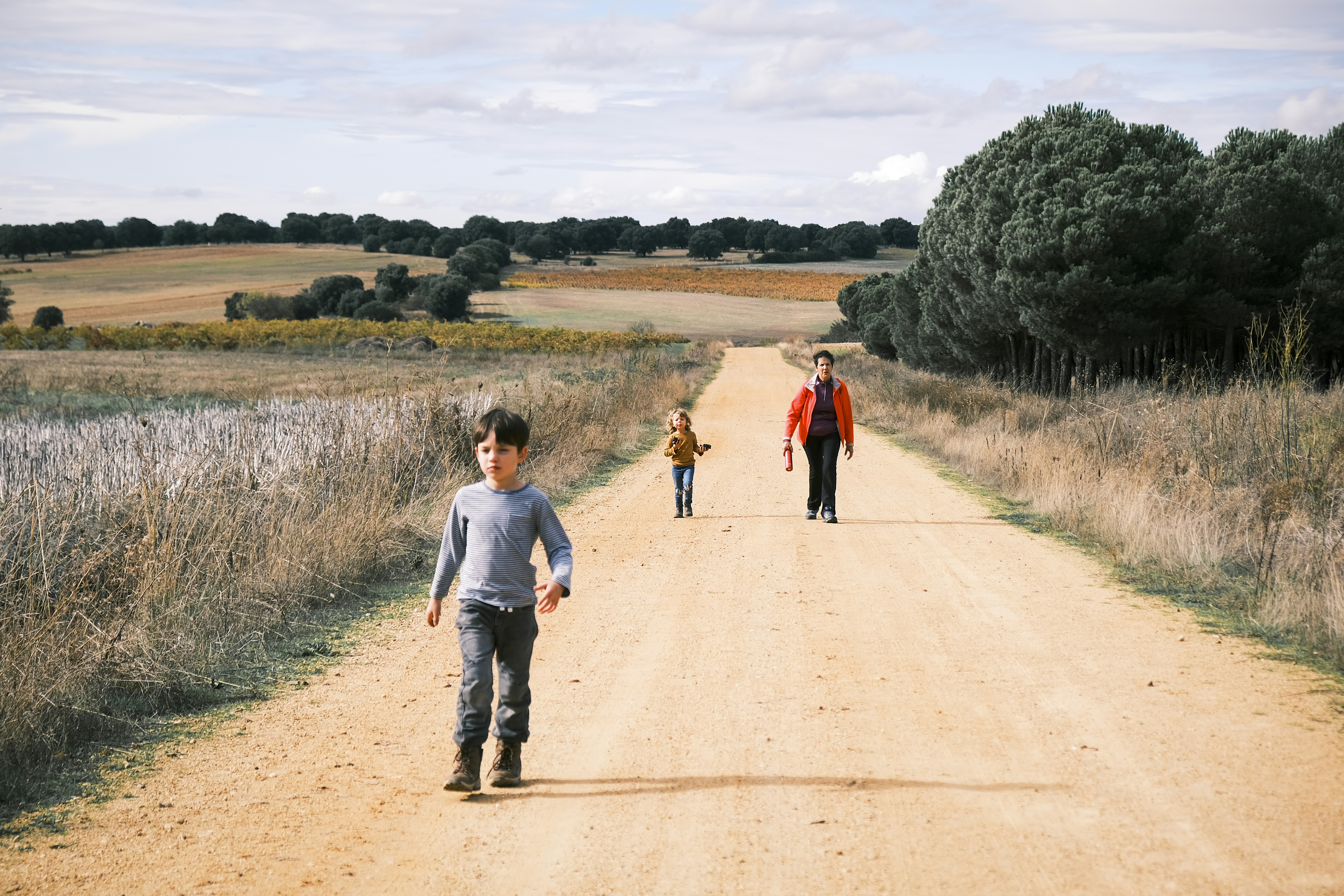 3人の子どもが土の道を歩いている