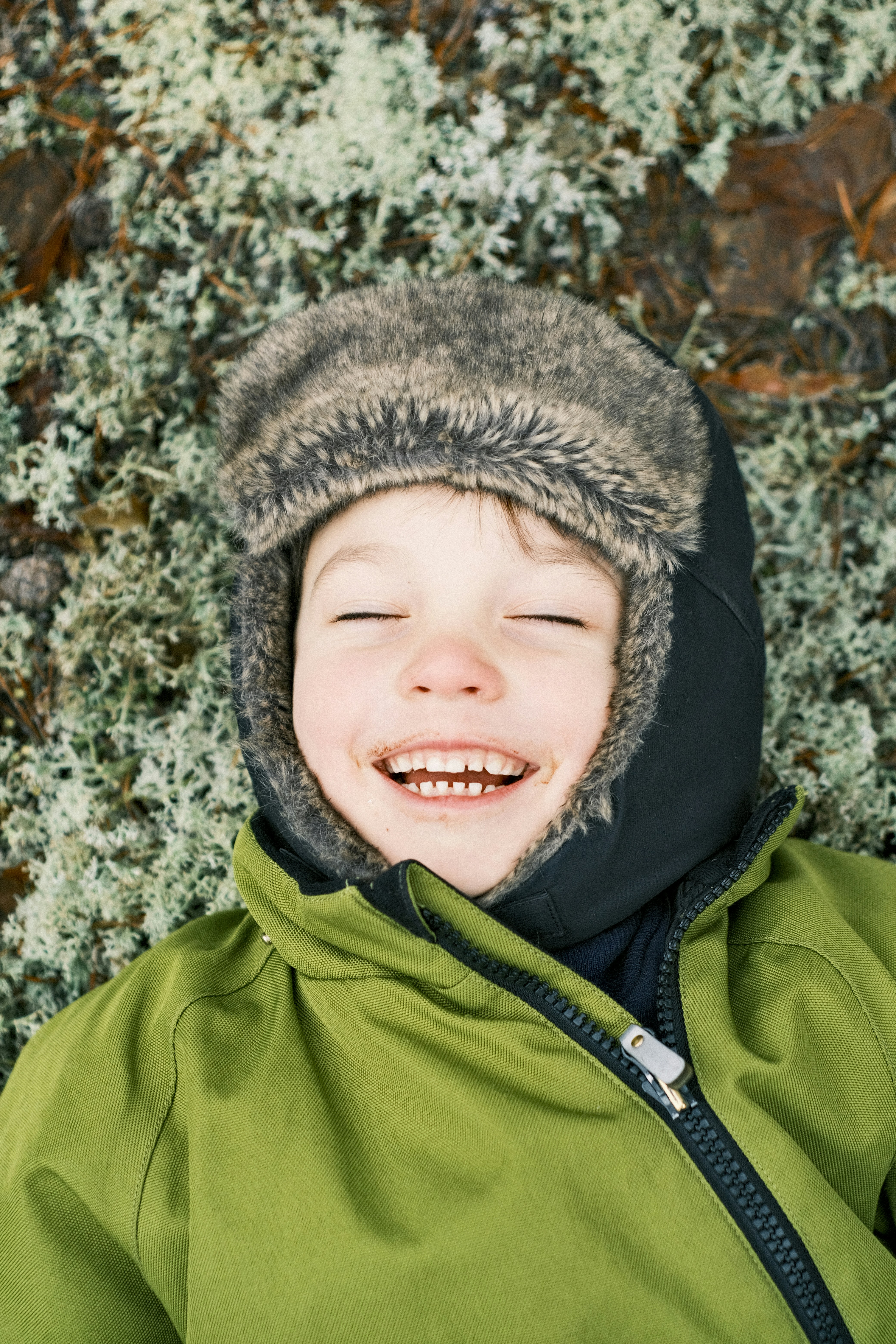 冬の帽子をかぶった幸せな子供が苔の上に横たわっている。