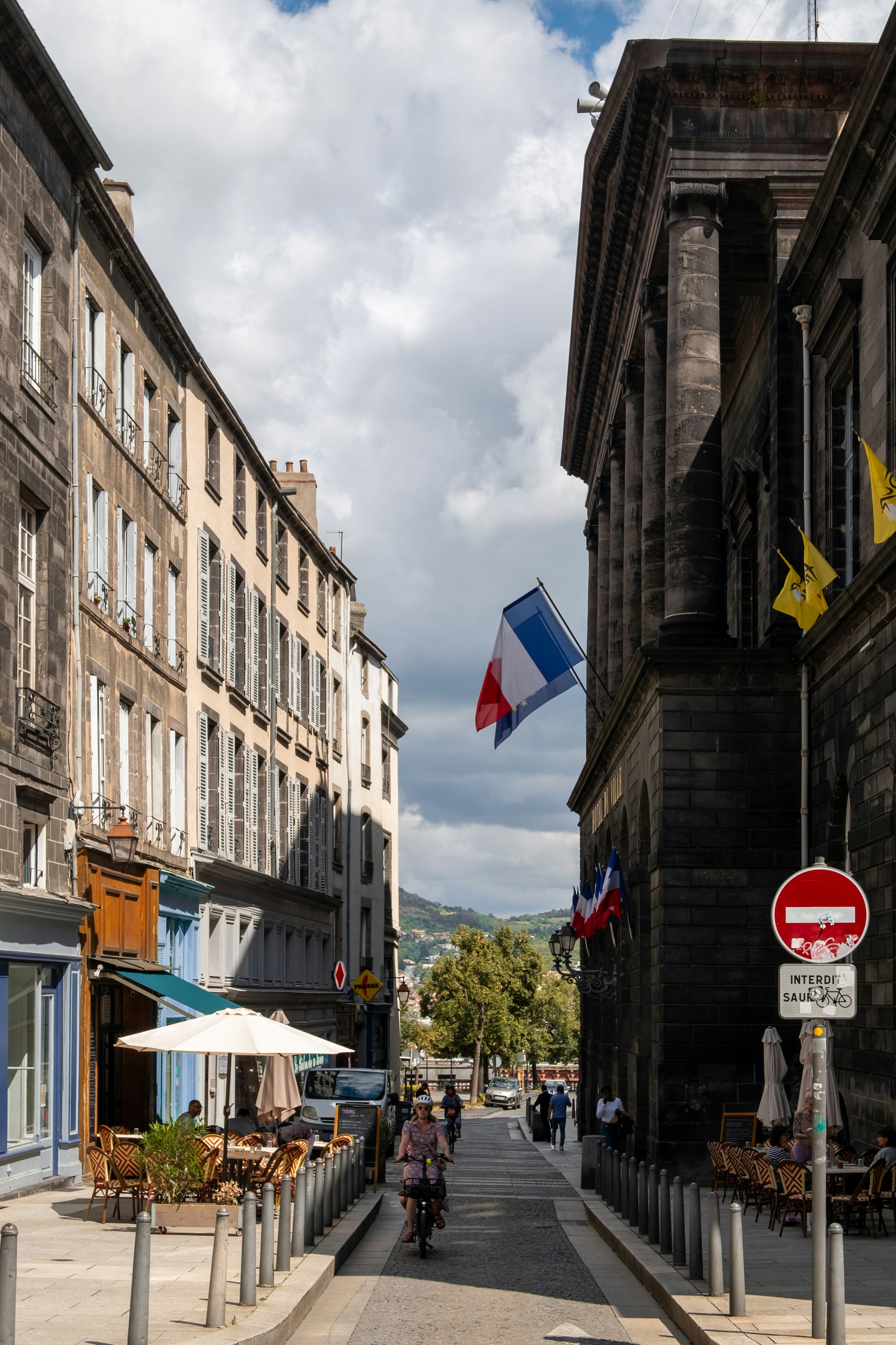 French flags fly on a street with buildings and people.