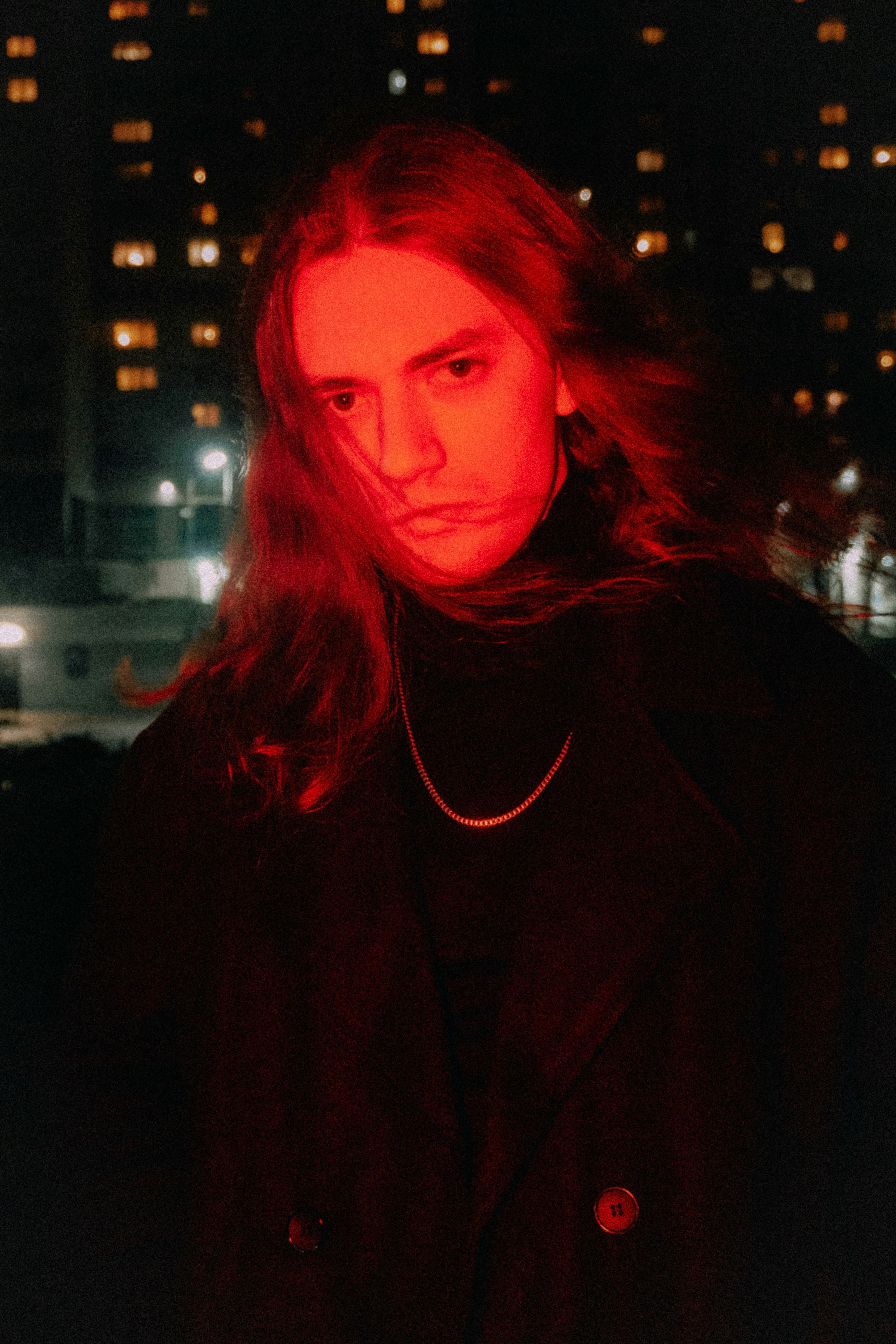 Man with long hair illuminated by red light at night.