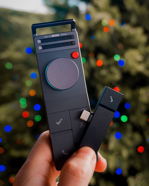 Hand holding a modern black device with colorful bokeh lights.