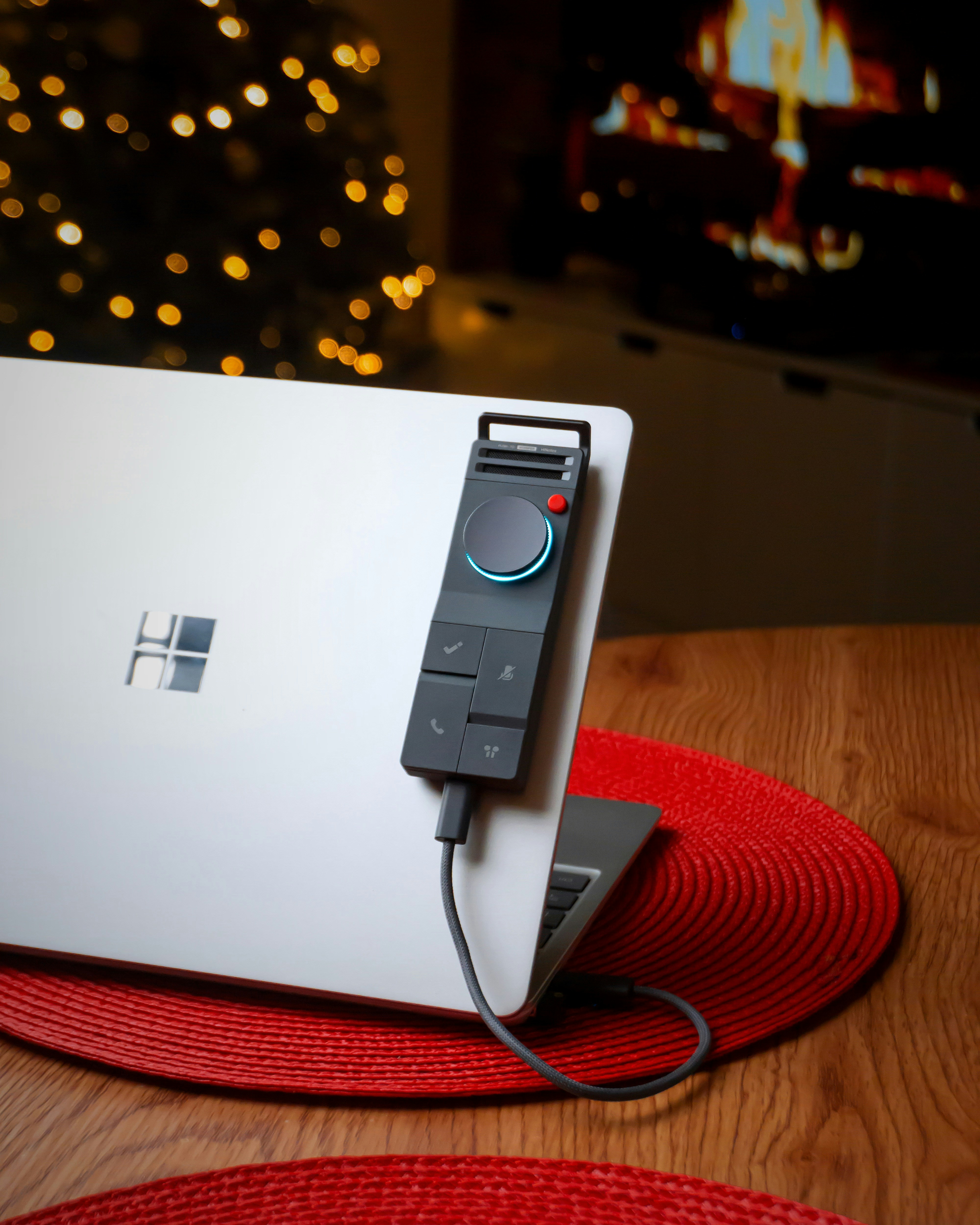 Laptop with a device attached, festive lights in background.