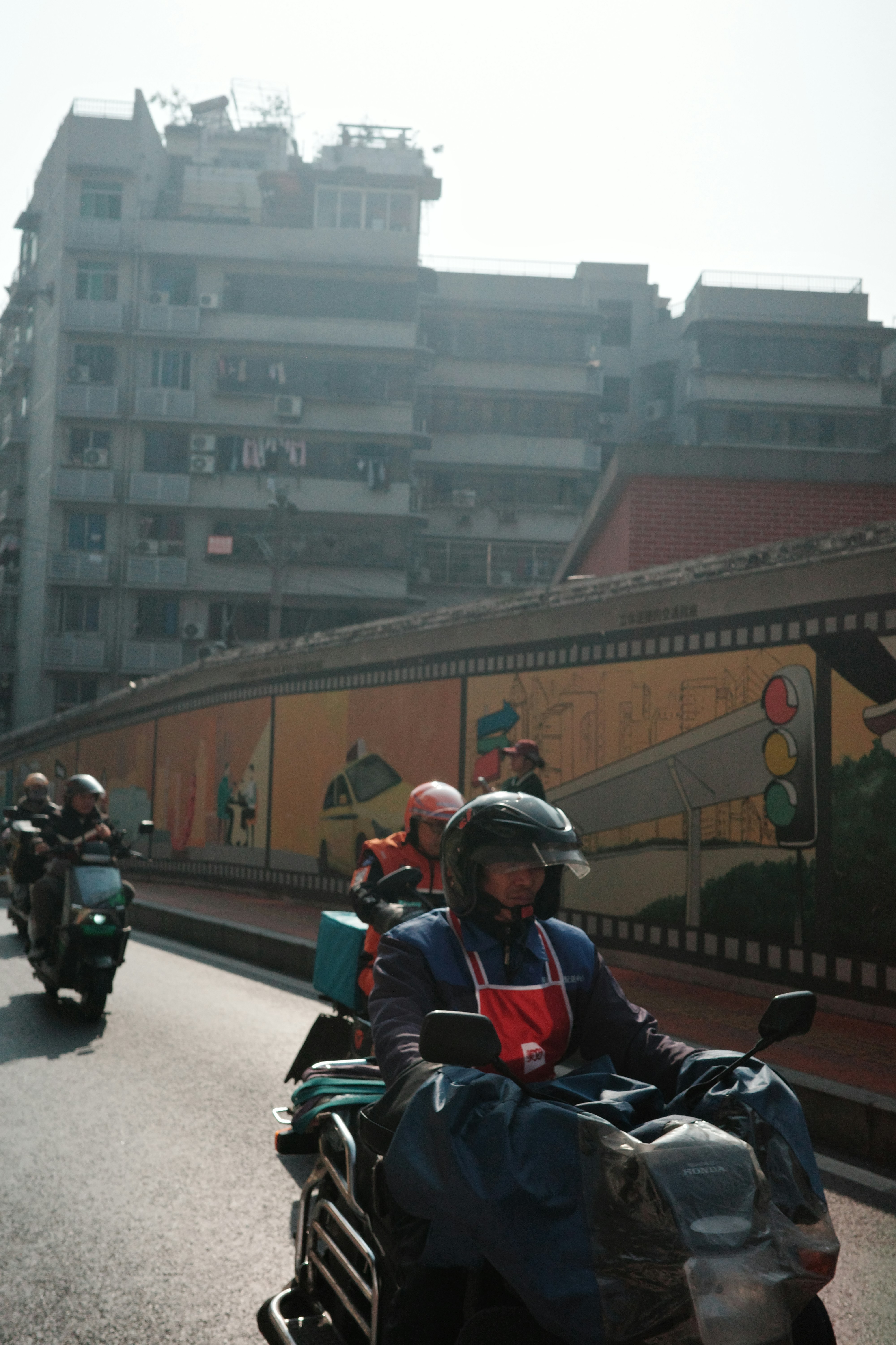 Des motards passent devant une fresque murale accrochée au mur.
