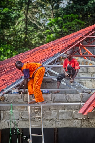 Two men working on a red metal roof