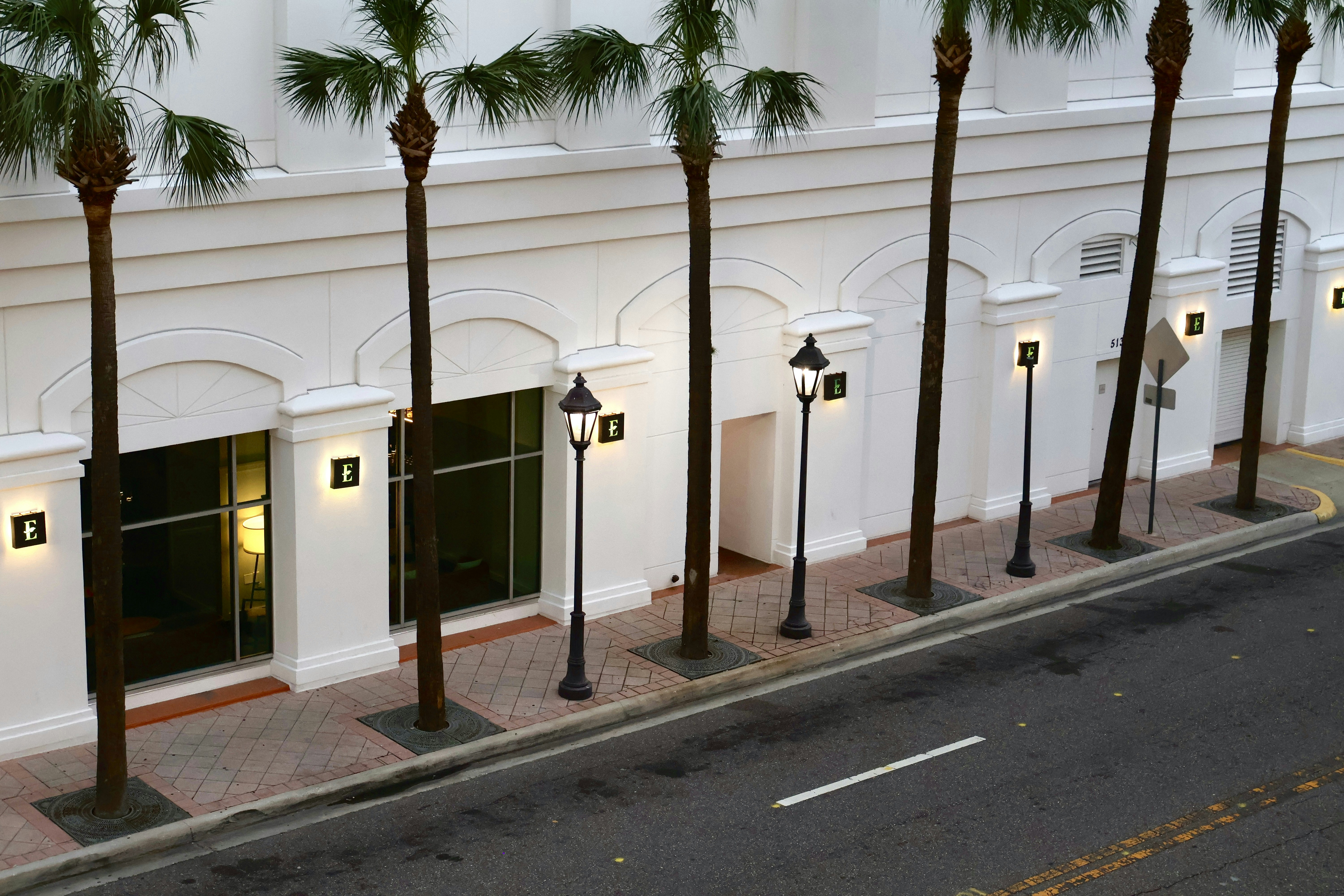Palm trees line a white building with streetlights.