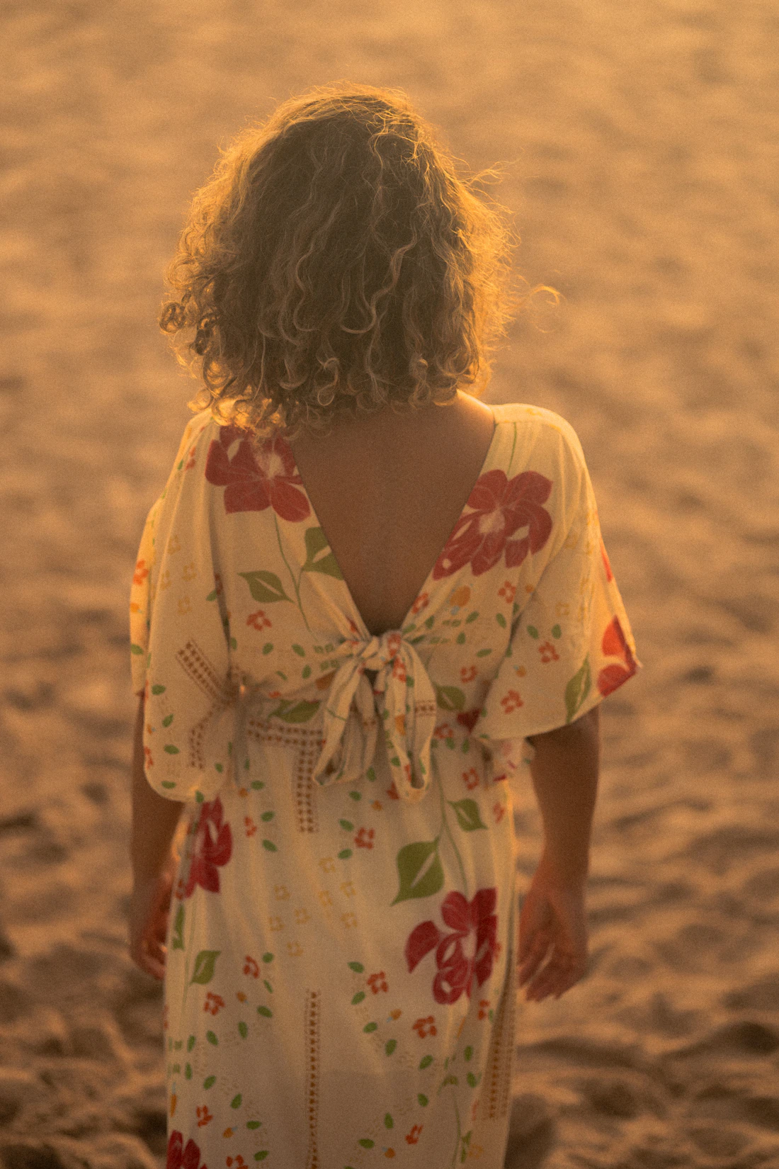 Model in a marigold floral kaftan on golden sand at sunset