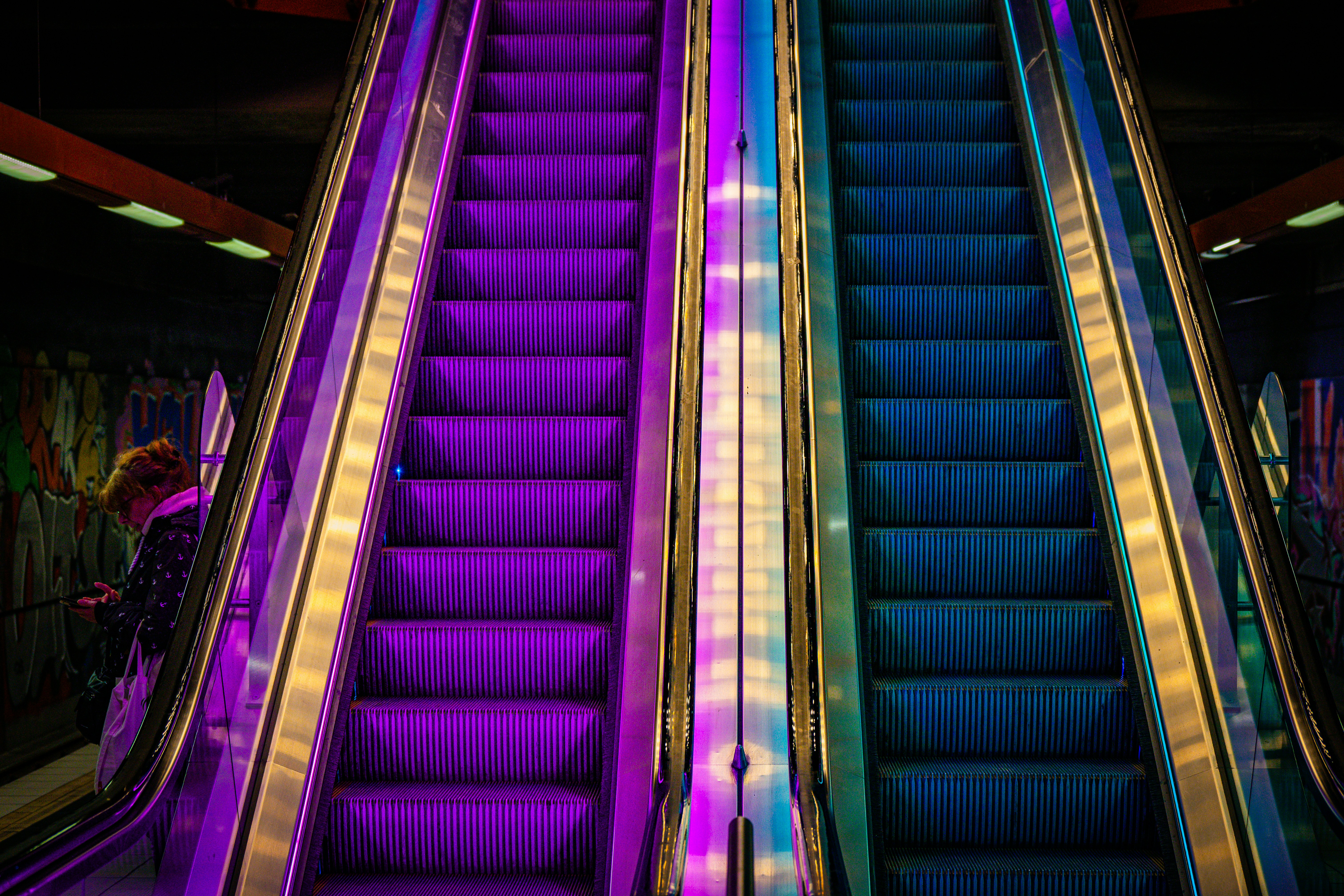 Two escalators illuminated with purple and blue lights.