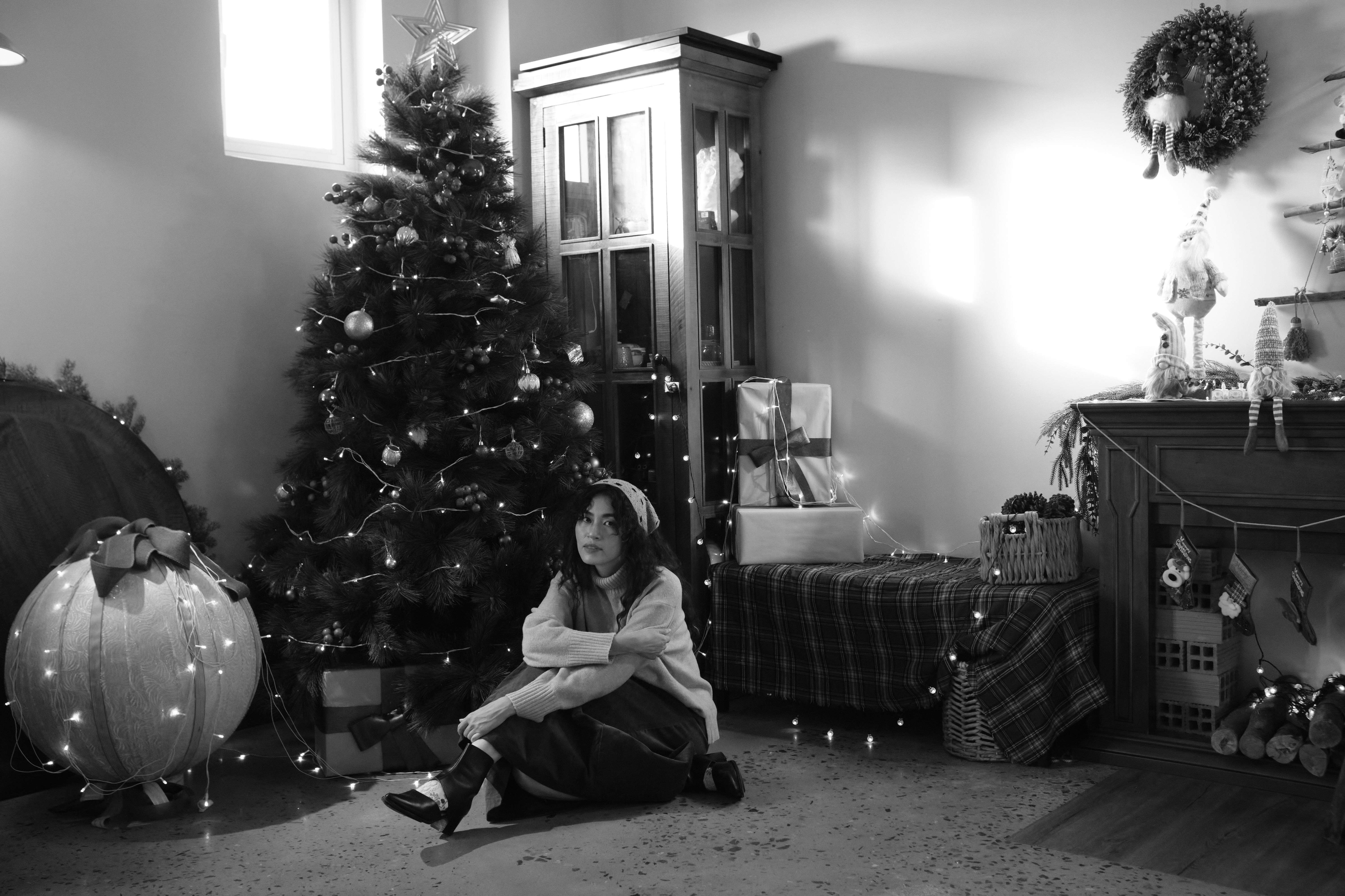 Chica sentada junto a un árbol de Navidad decorado y regalos.