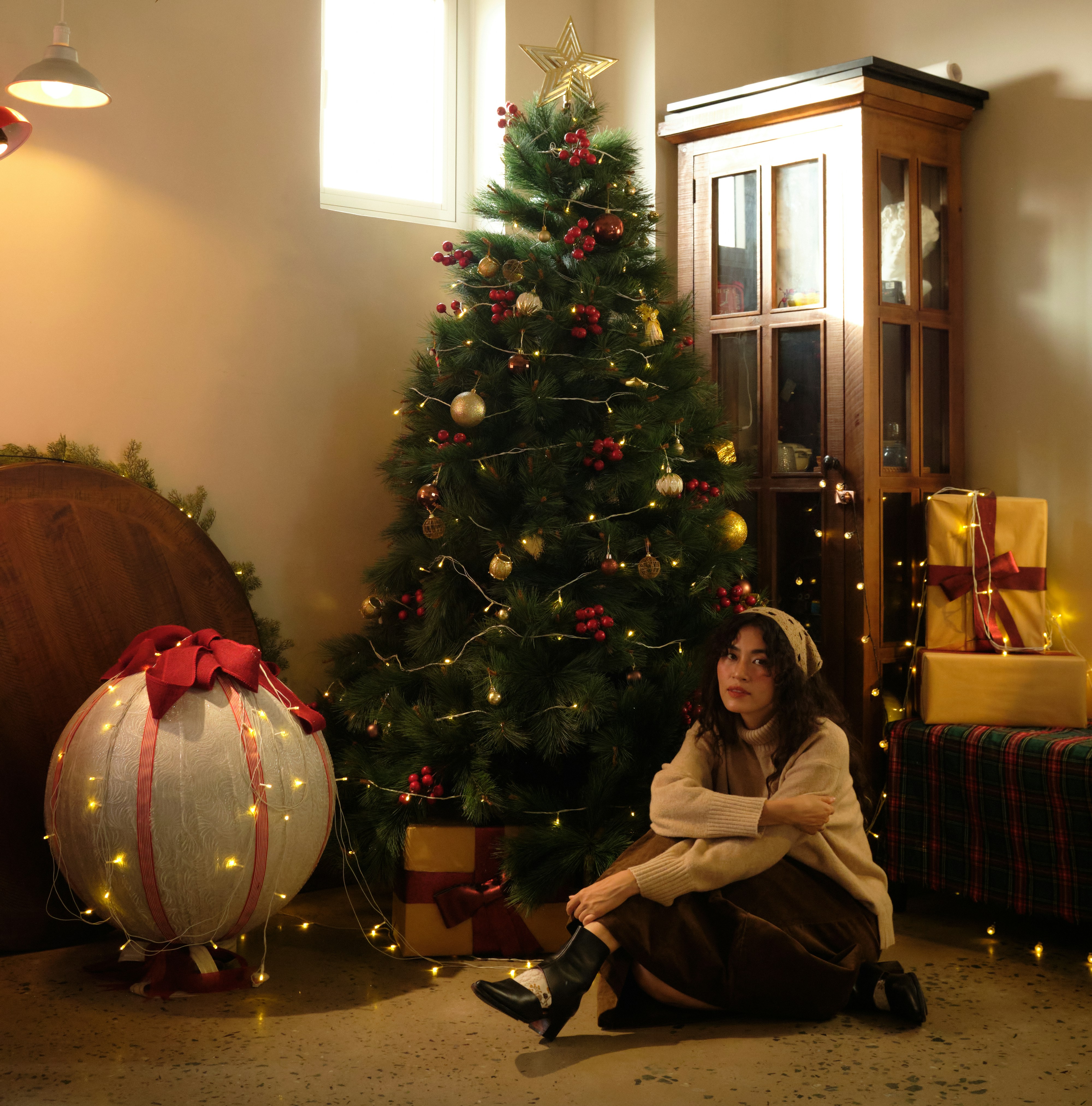 Young woman sitting near a decorated christmas tree.