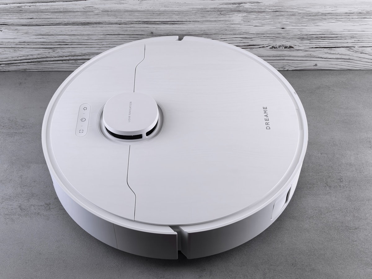 A white robot vacuum cleaner on a grey floor.