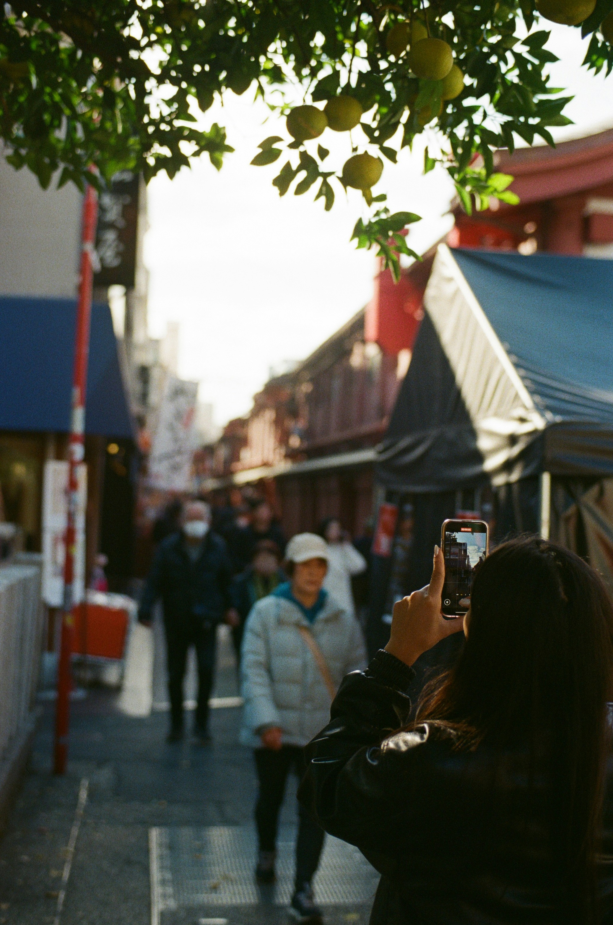 Person taking a photo on a street with buildings.