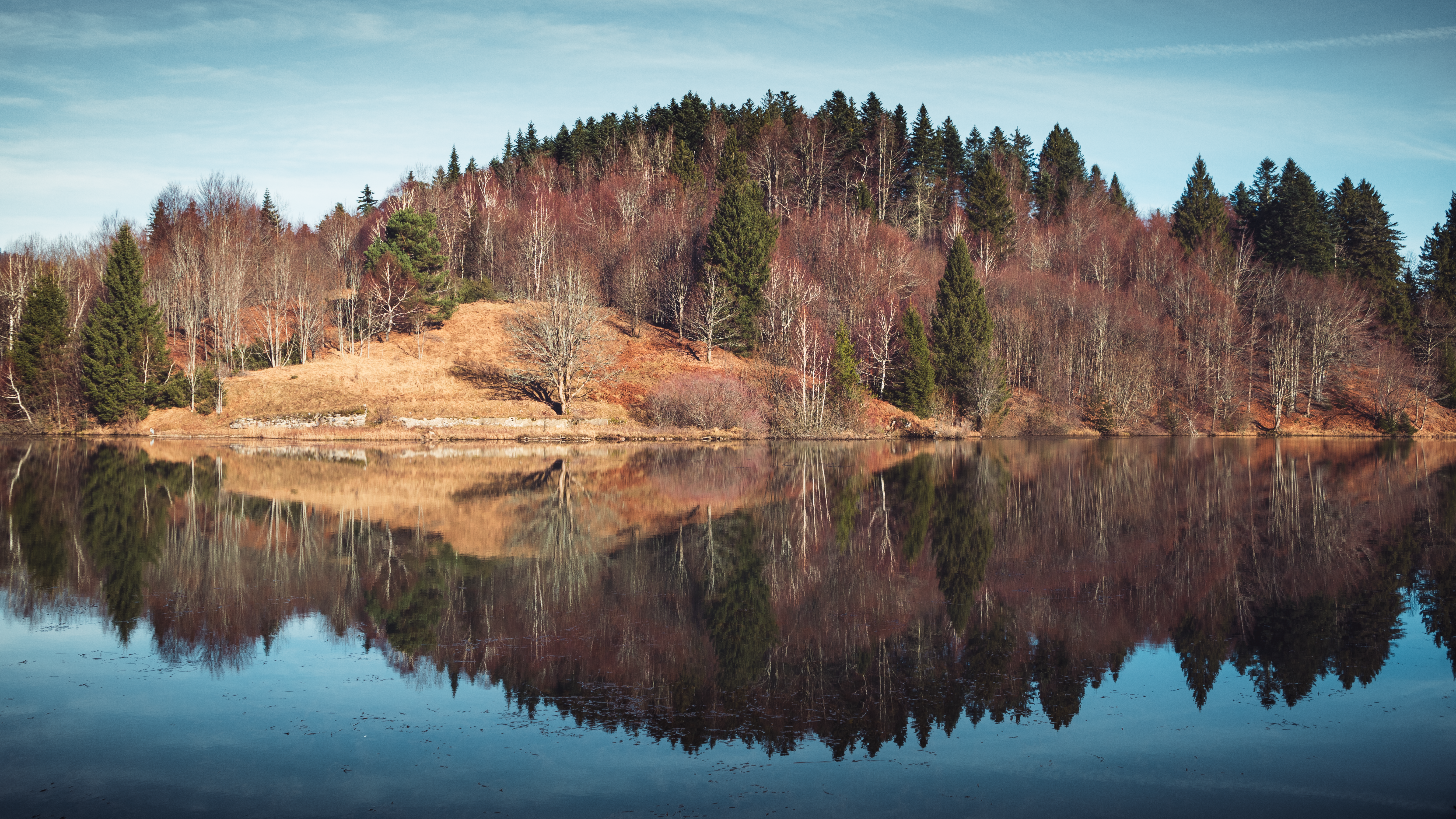 Calm lake reflecting a hill with bare trees