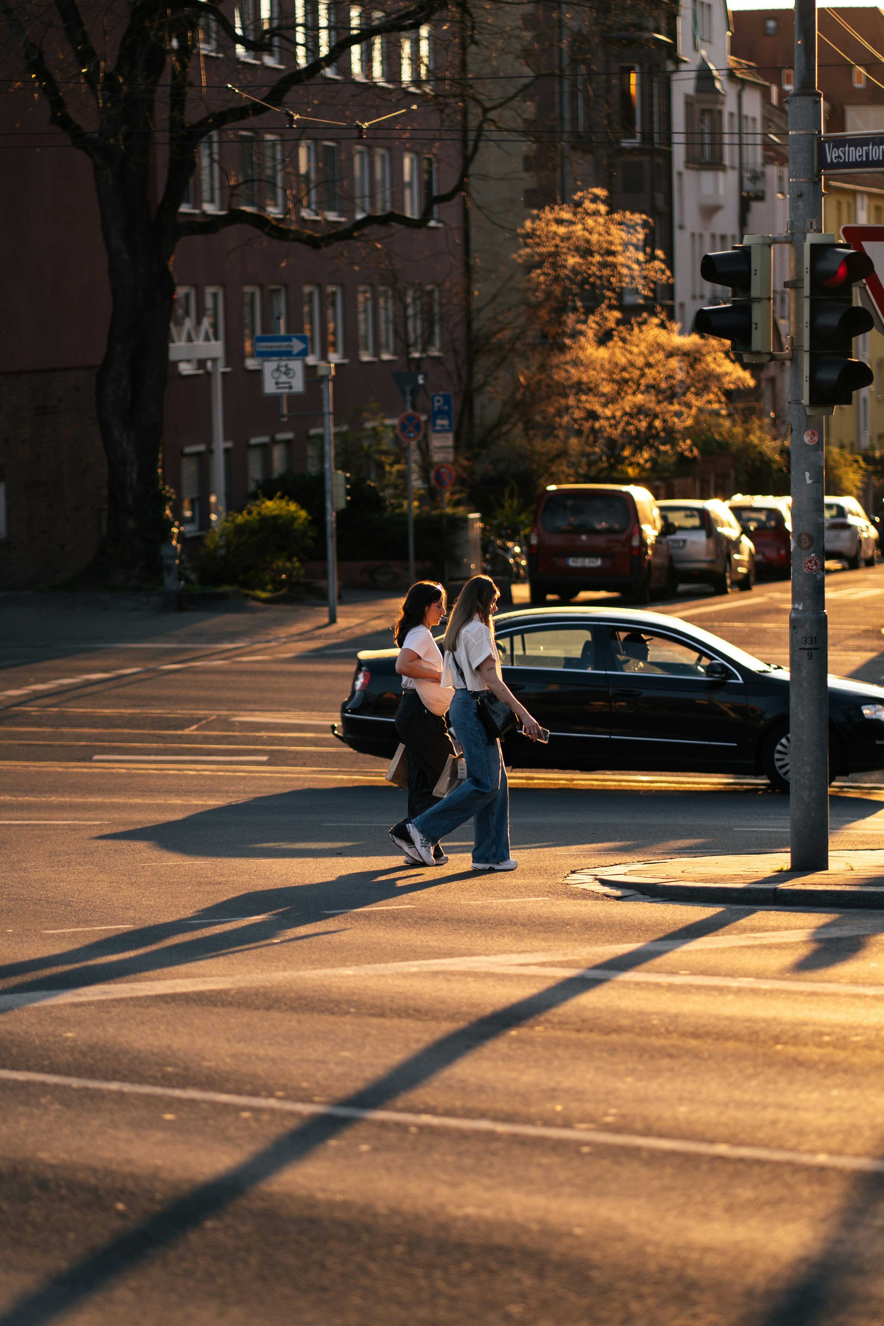 Two women cross a sunlit street at an intersection.