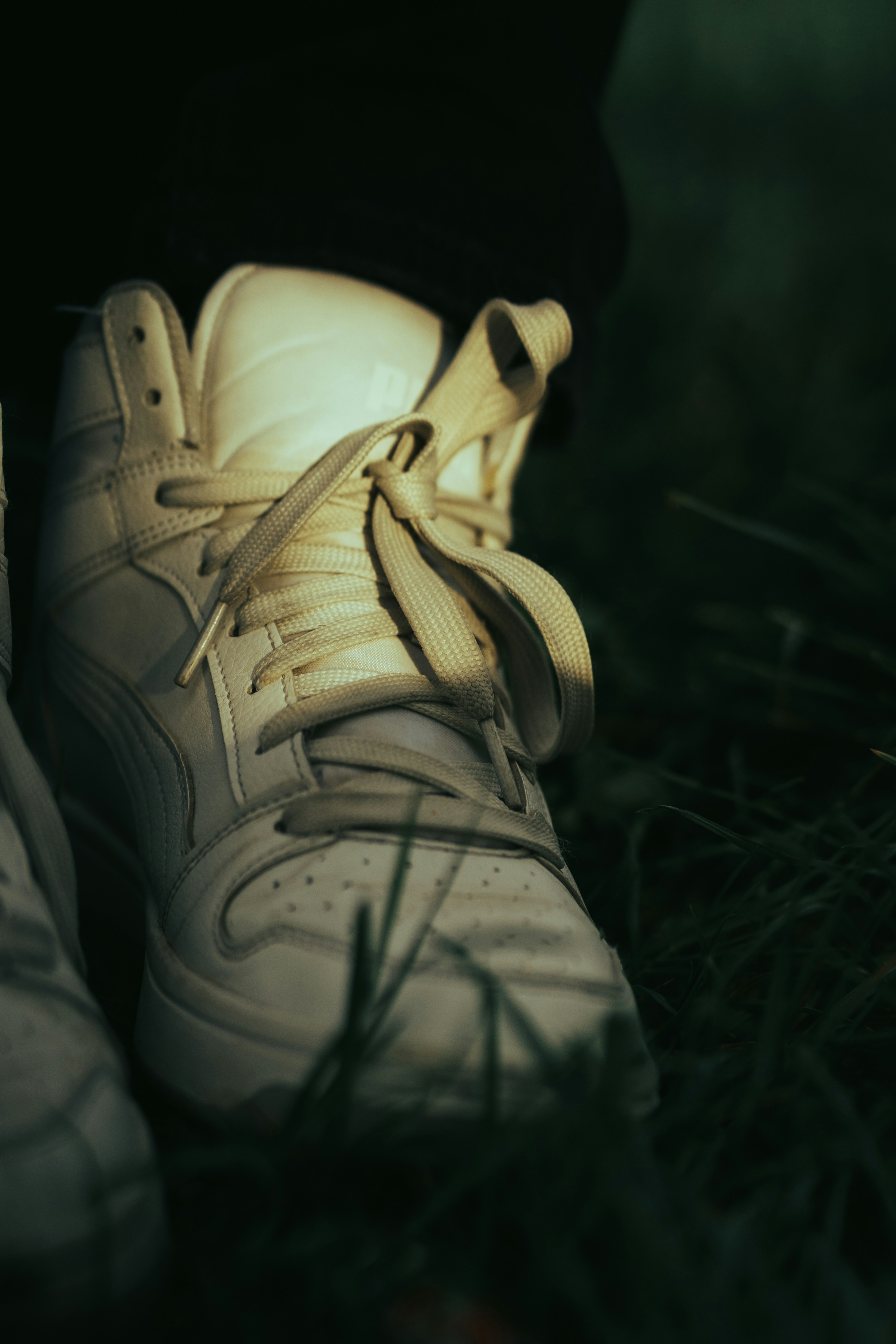 White high-top sneakers resting on green grass.