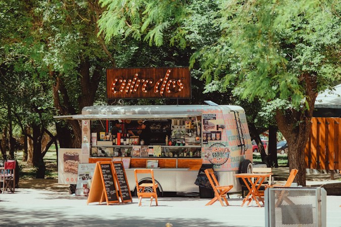 A food and beverage truck set up with outdoor seating under shade trees
