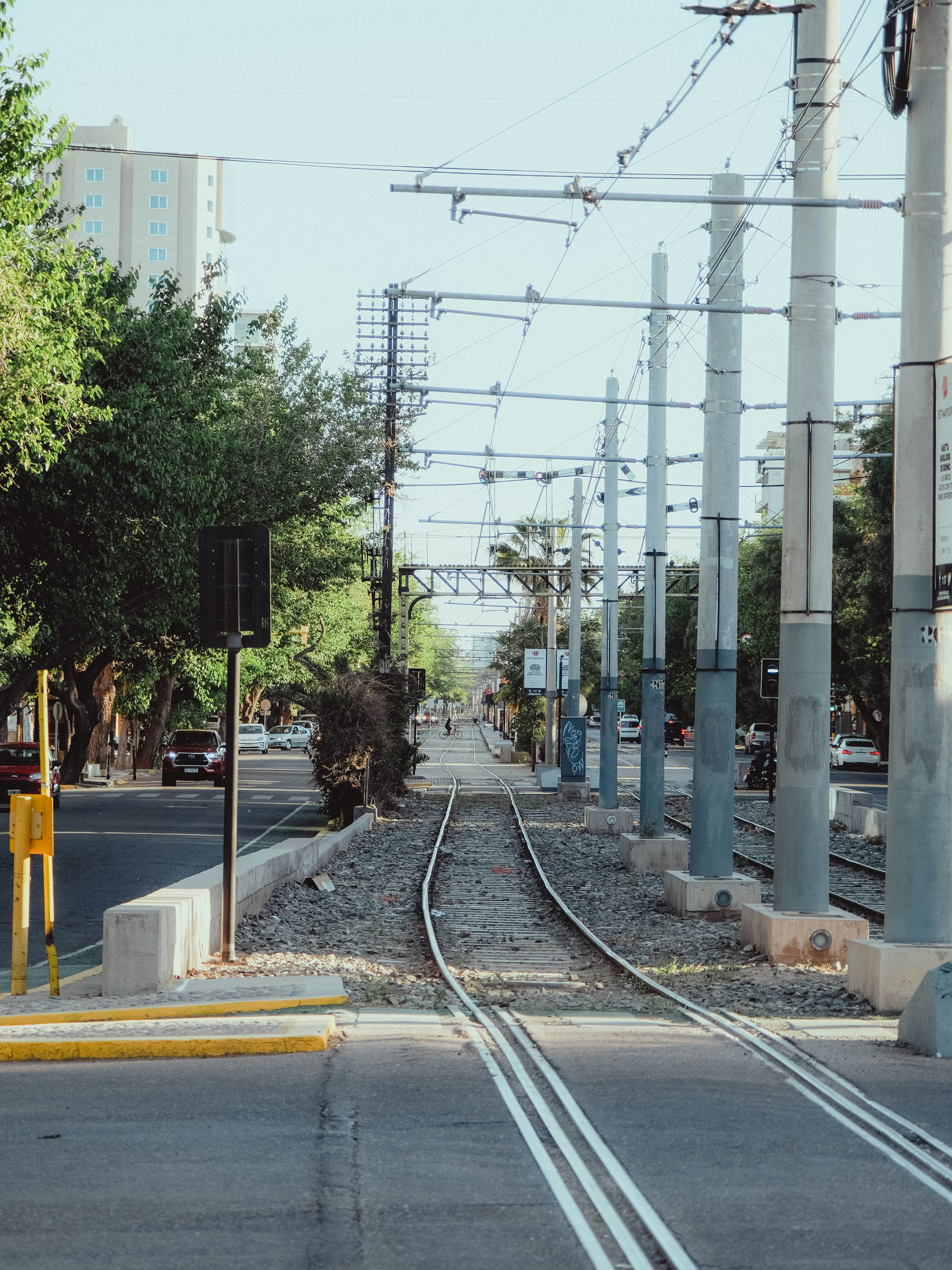 Train tracks run through a city street with overhead wires.
