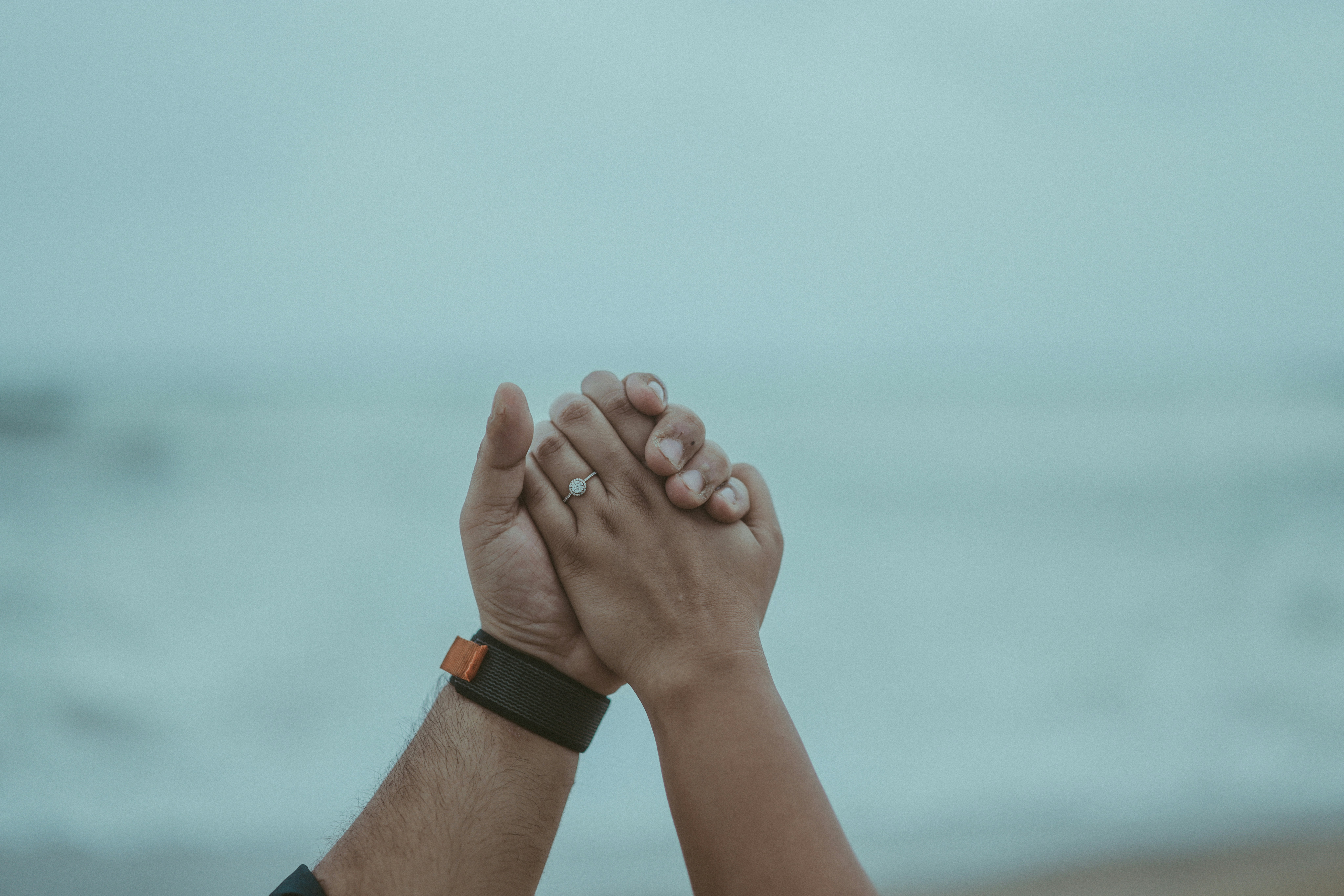 Couple holding hands with engagement ring on beach