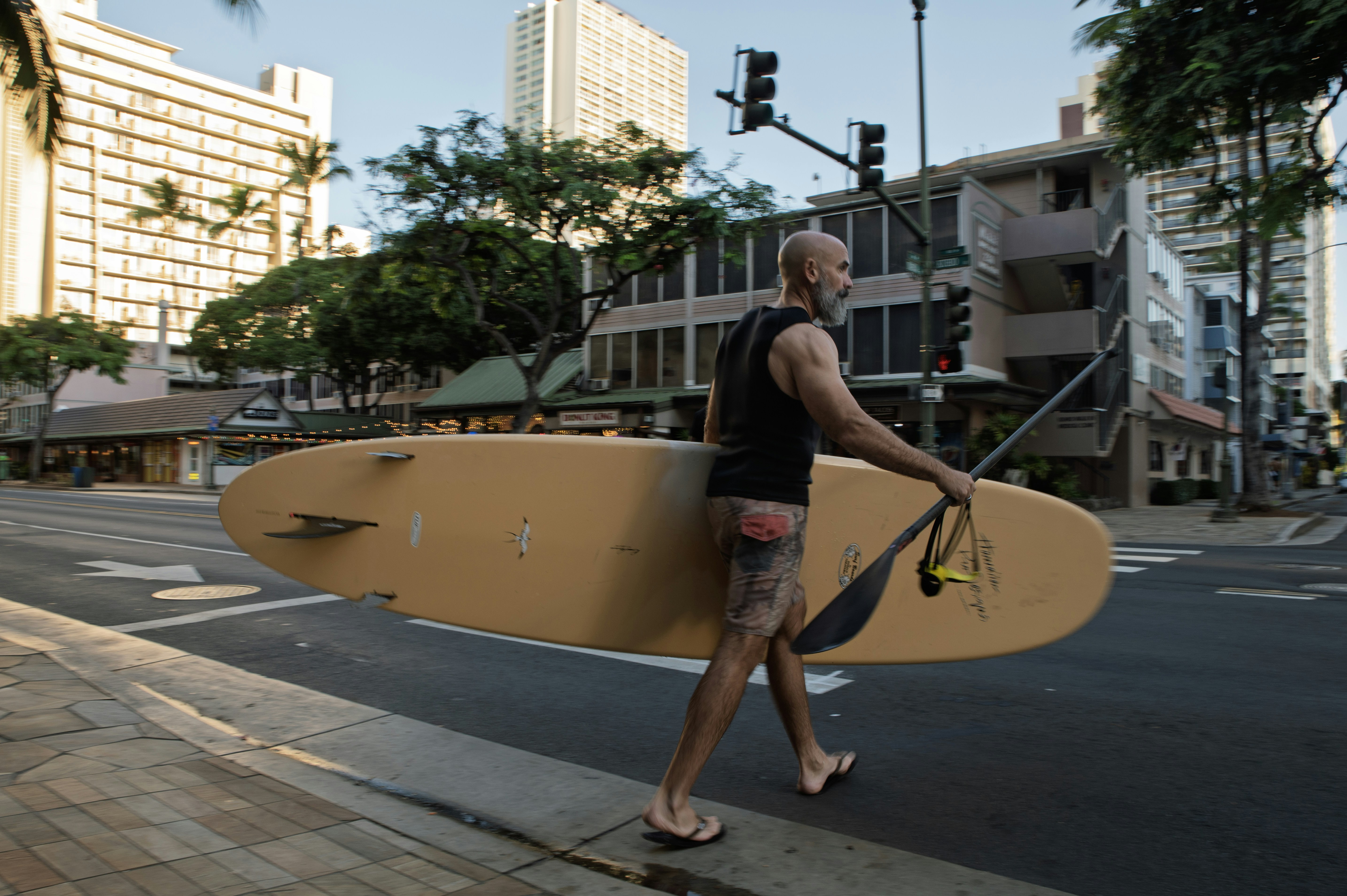 Man carrying a surfboard down a city street.