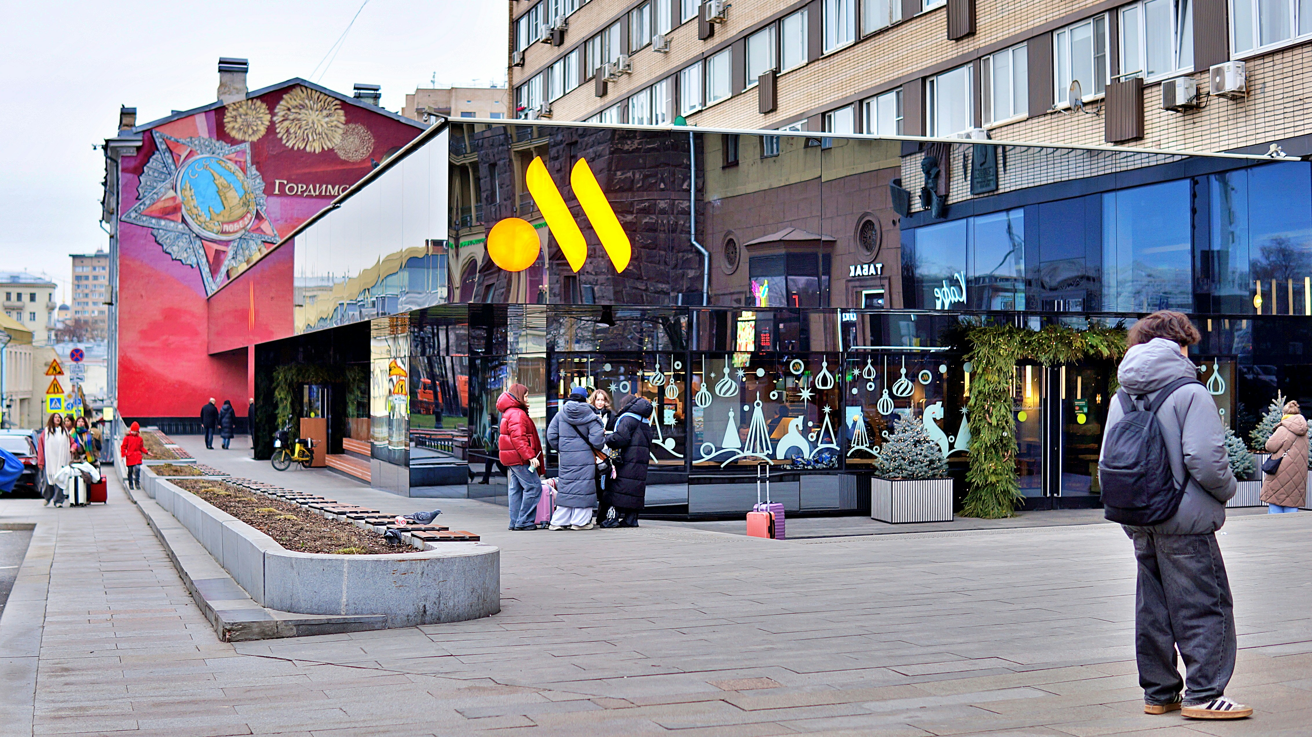 Modern building with large yellow logo and people walking.